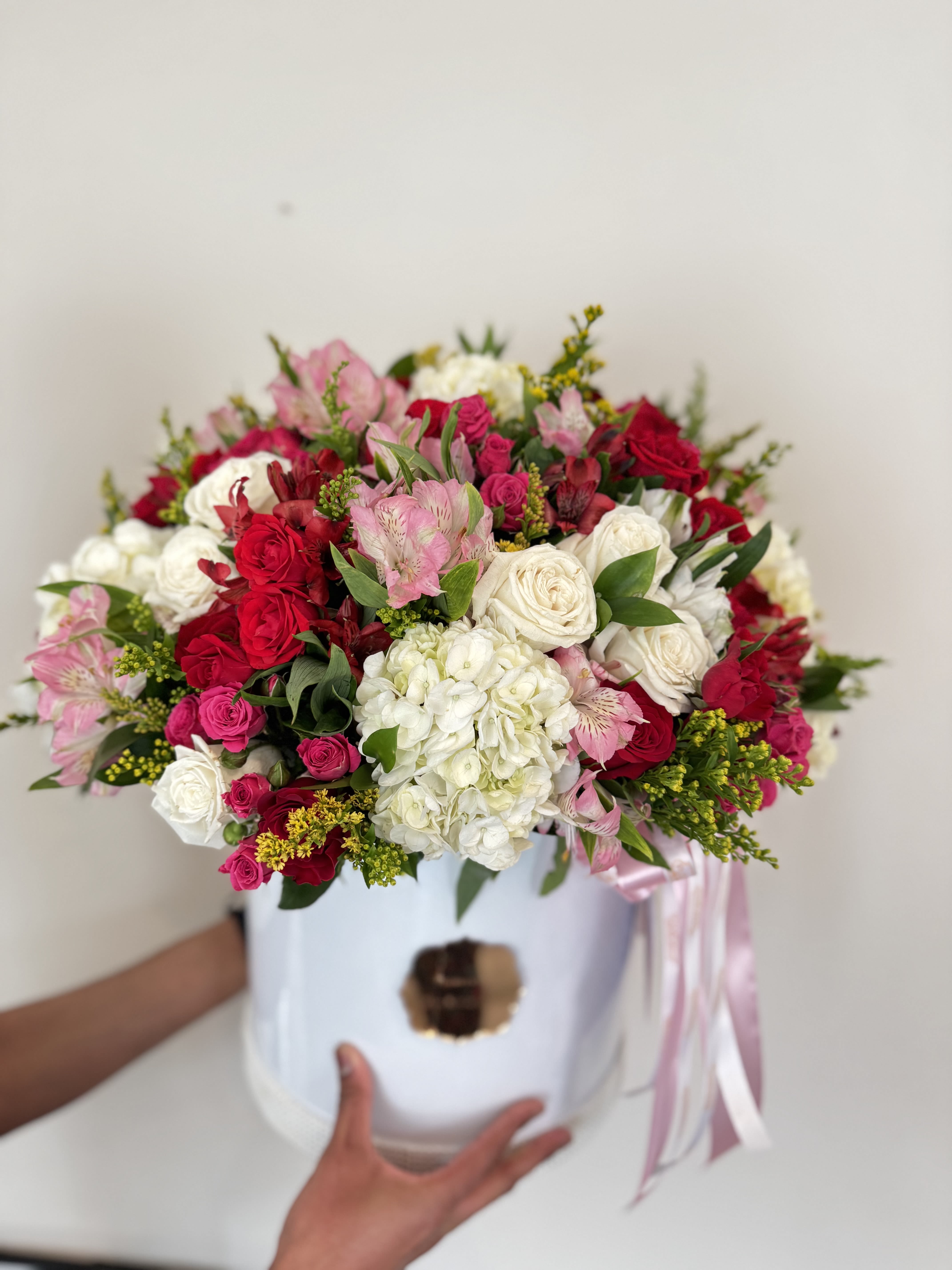 Mixed pink, red, and white flower arrangement in a white hat box with ribbon