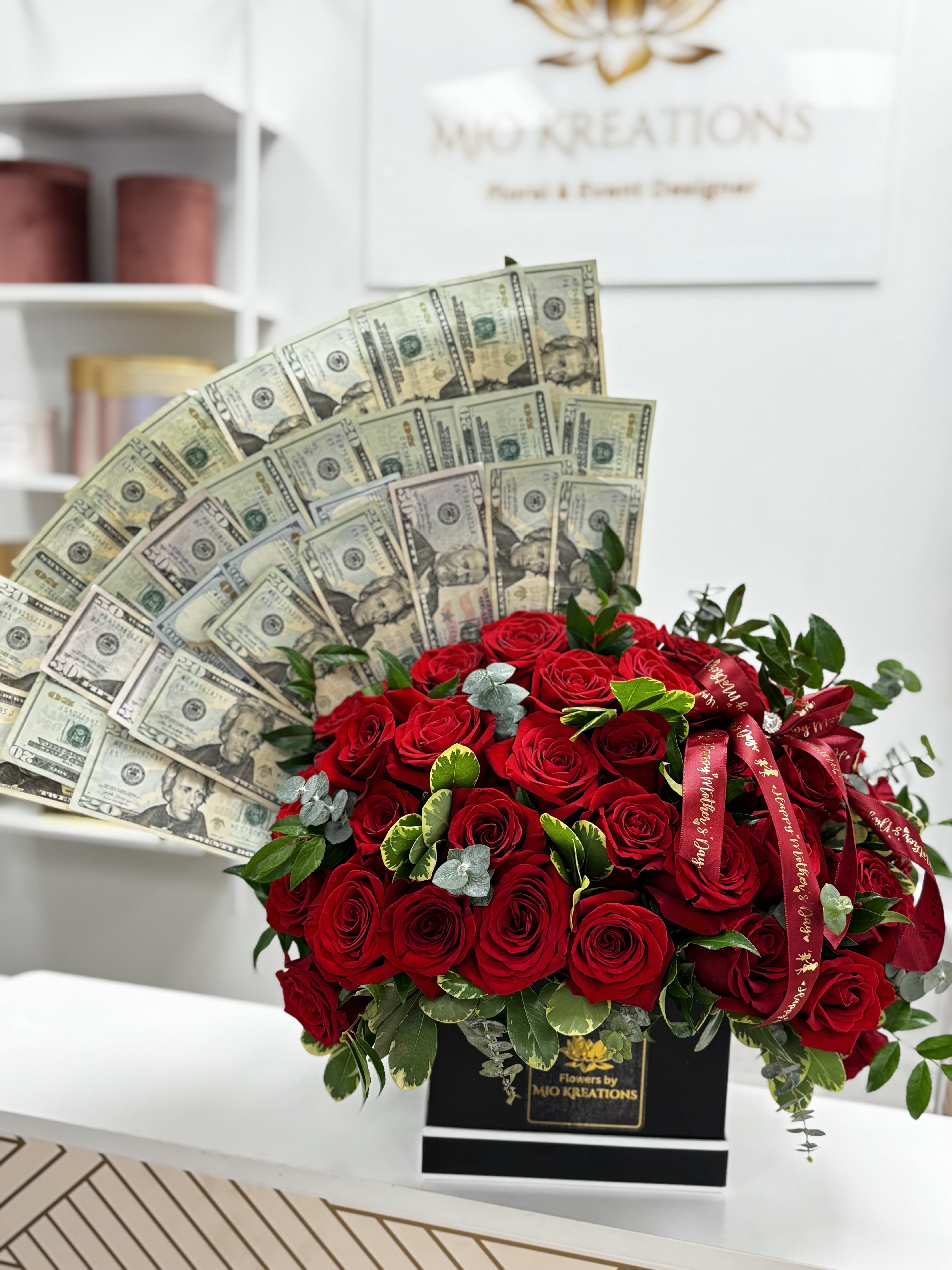 Red rose arrangement with fan-shaped dollar bills and ribbon in a black box