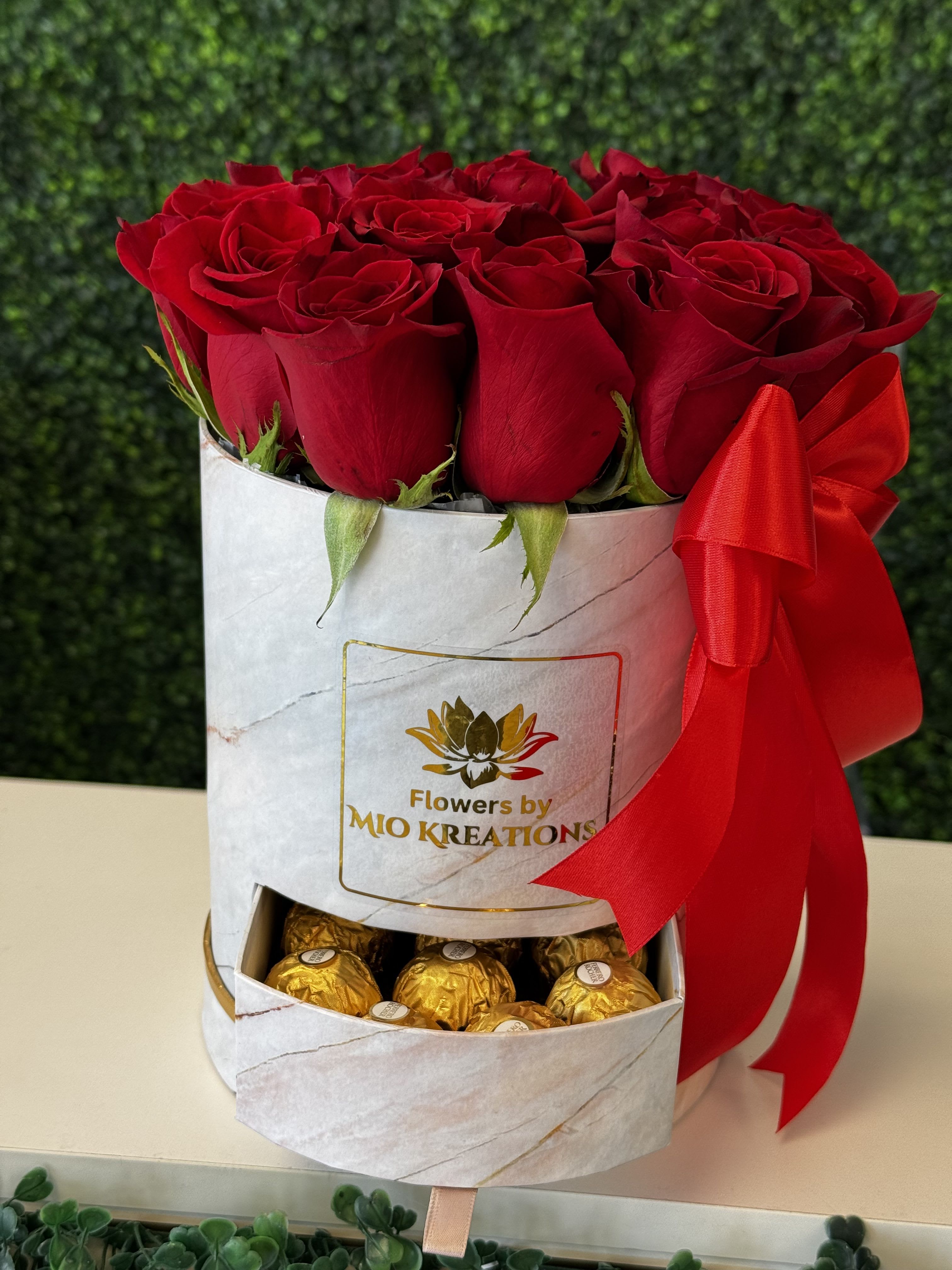 Red roses in a white gift box with gold chocolates and a red ribbon