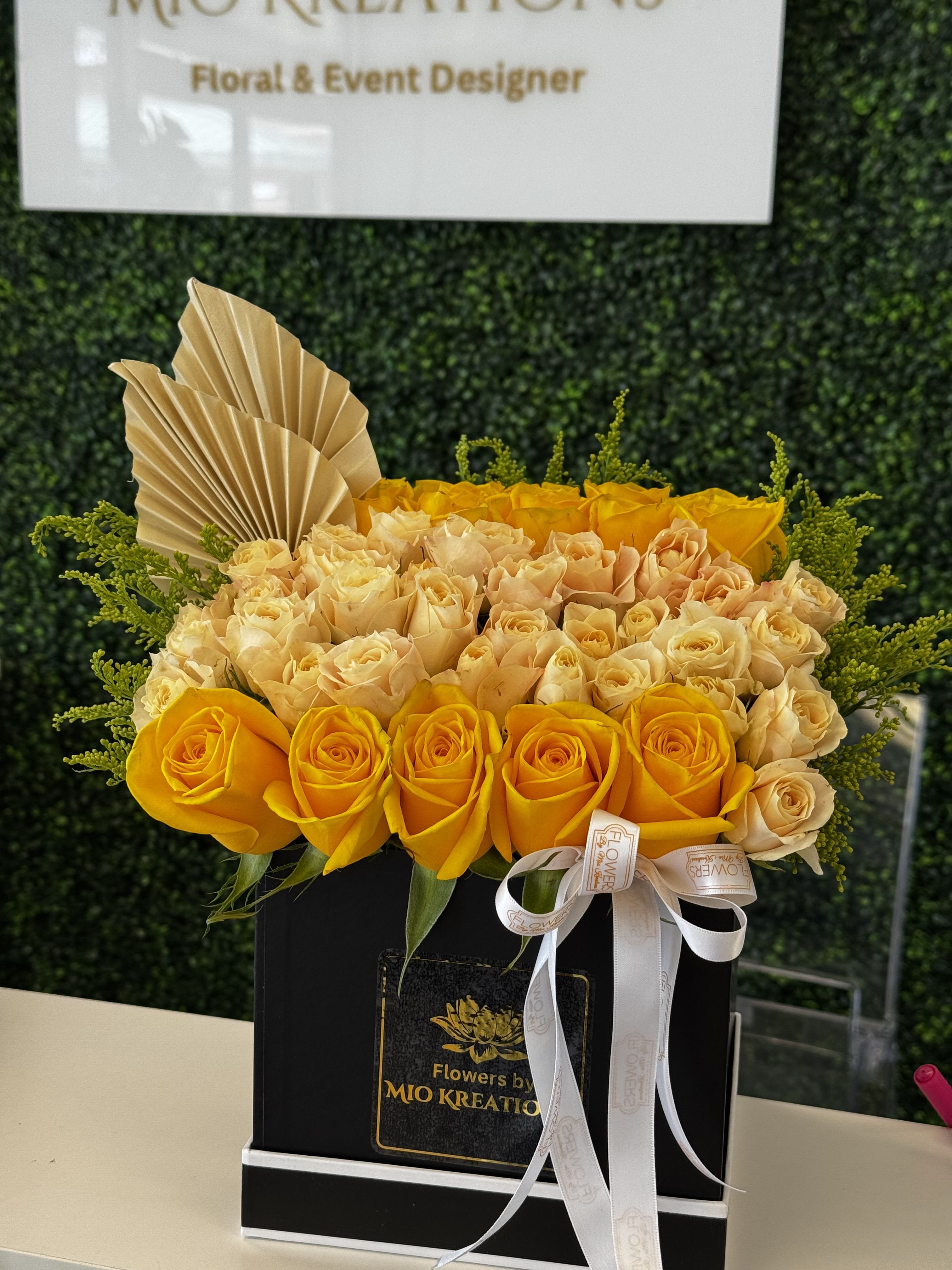 Yellow and cream roses arranged in a black box with a ribbon