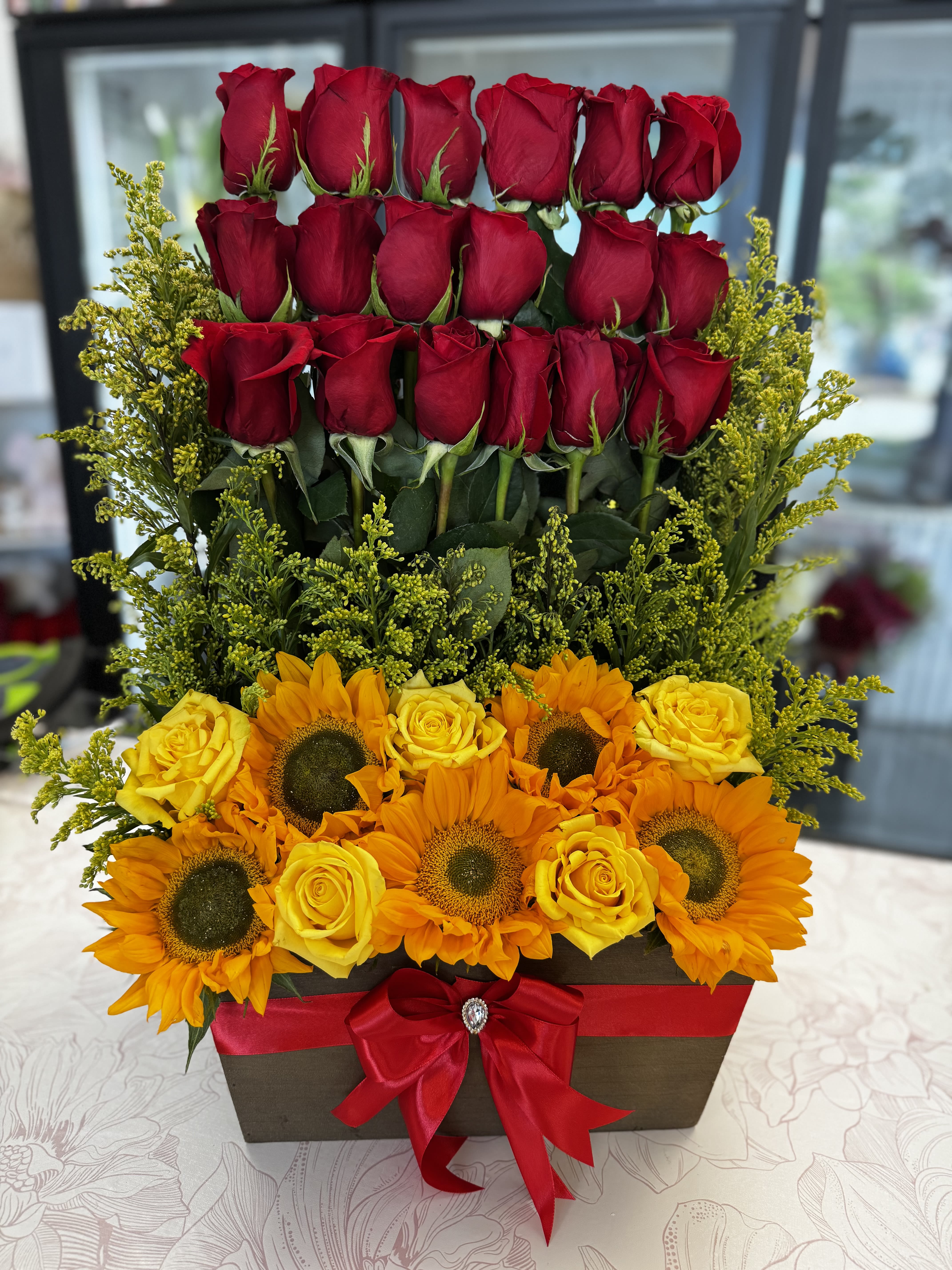 Tiered floral arrangement with red roses, yellow roses, and sunflowers in a box