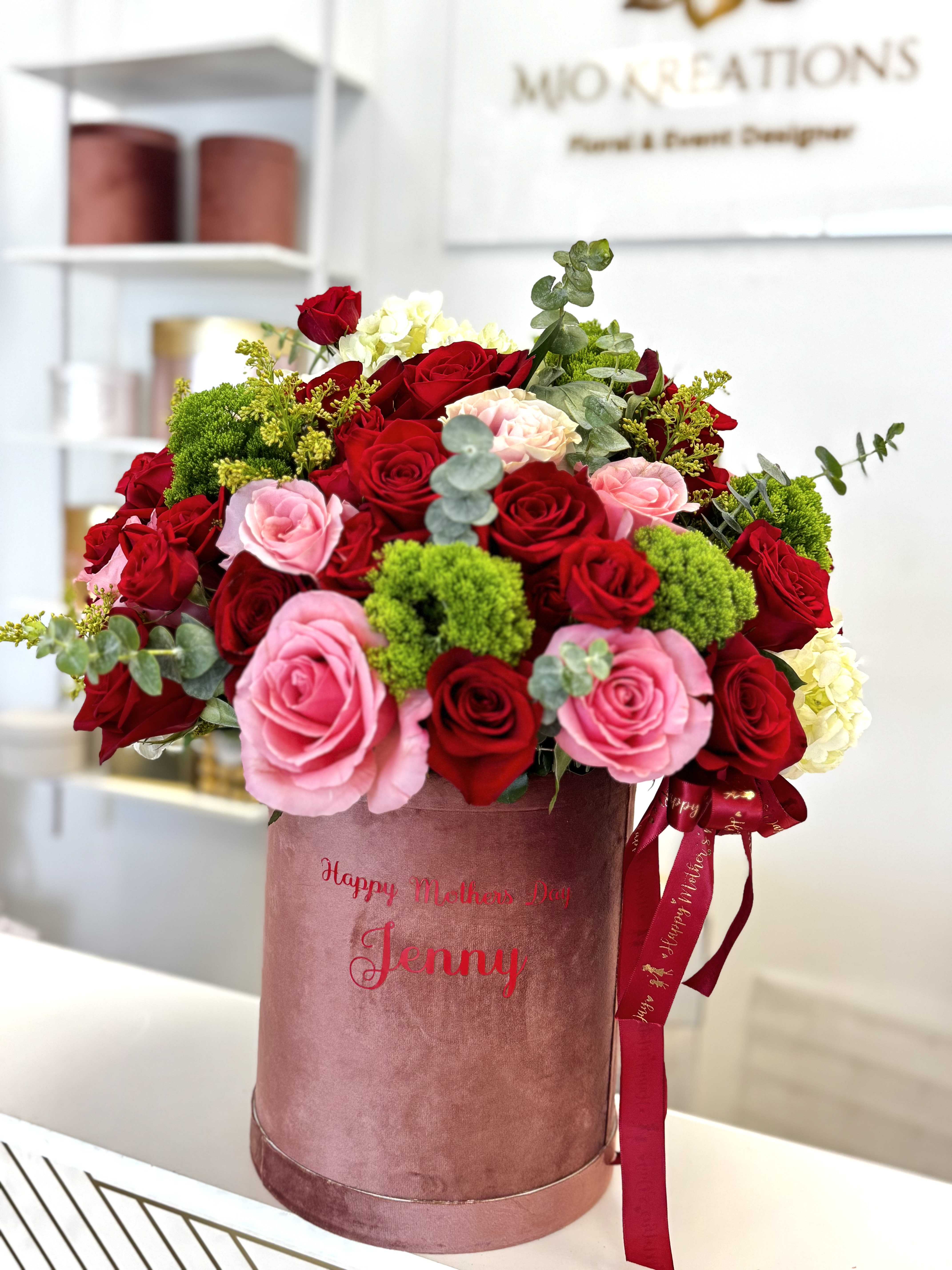 Red and pink roses arranged in a pink hatbox with ribbon