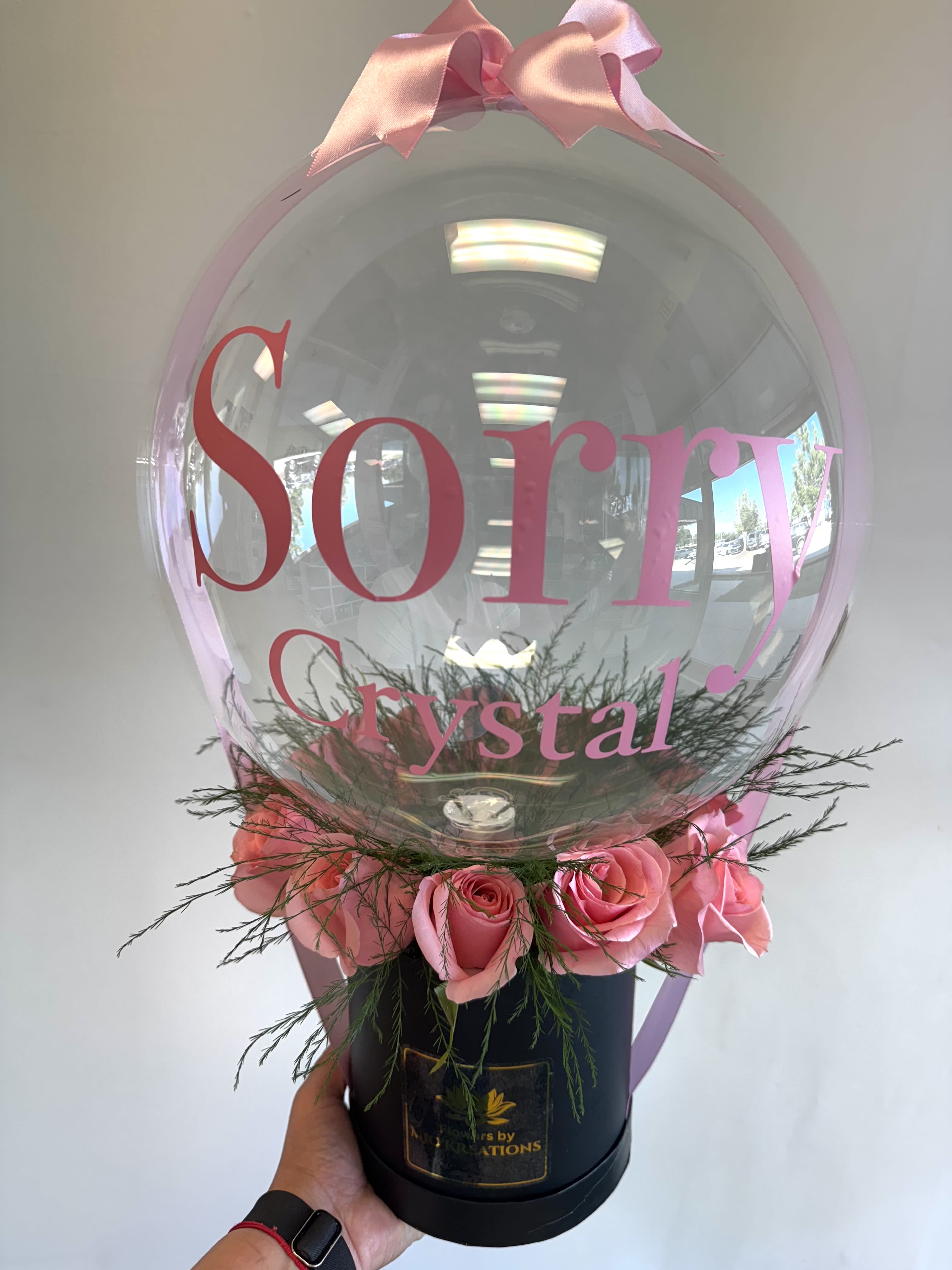 Pink roses arranged around a clear balloon with a pink bow
