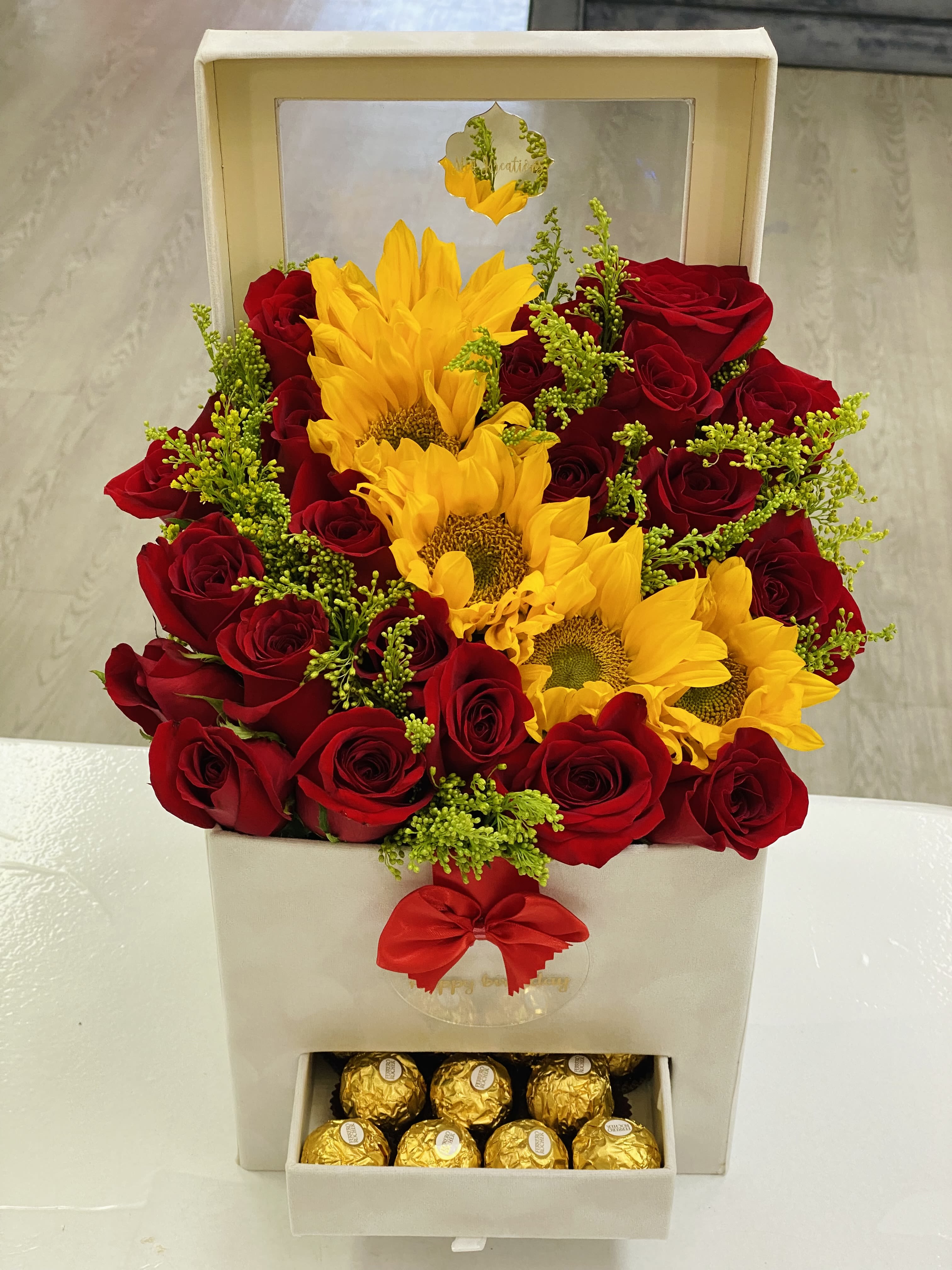 Red roses and yellow sunflowers in a gift box with chocolates