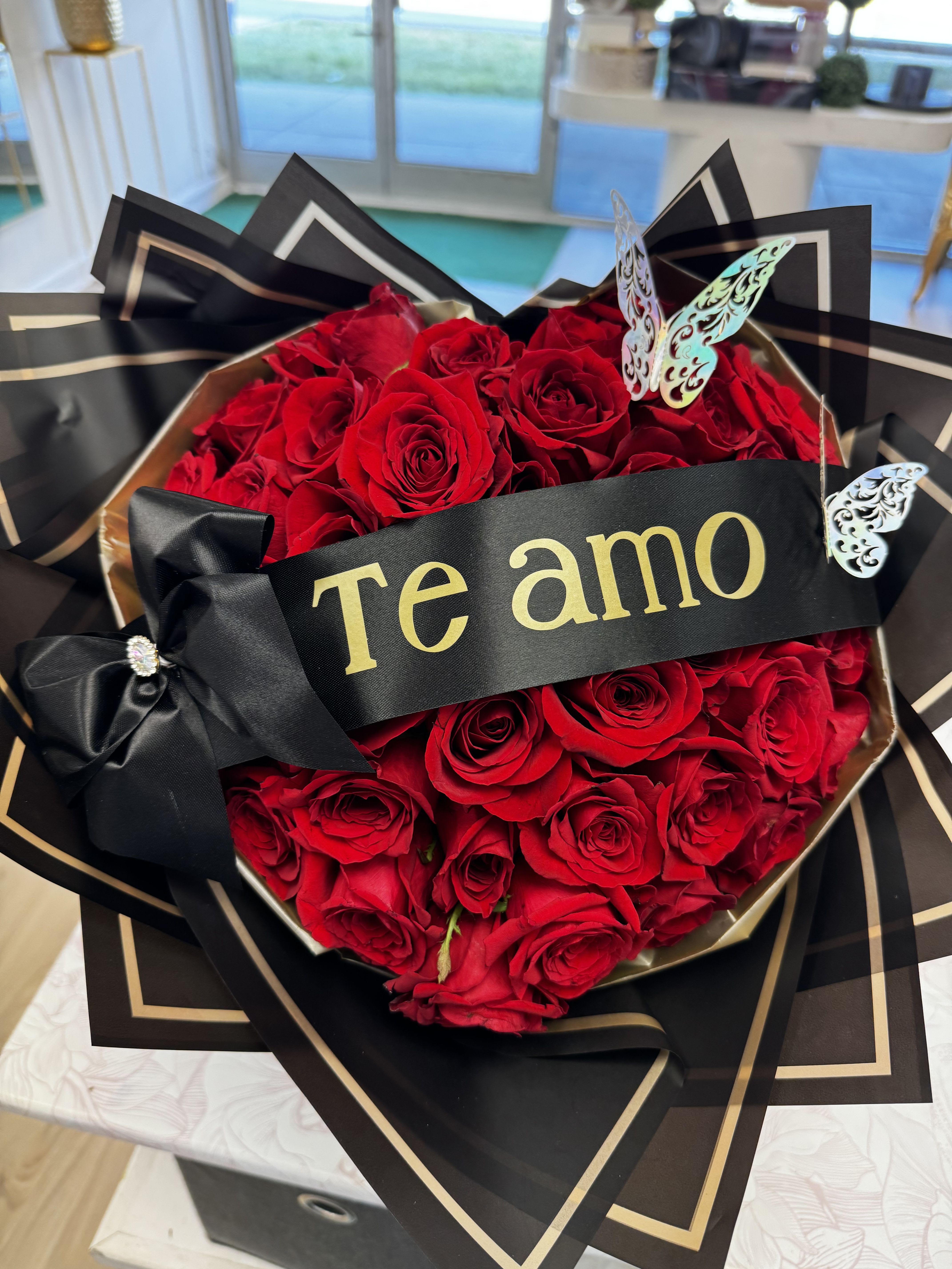 Heart-shaped bouquet of red roses with a black ribbon and "Te amo" banner