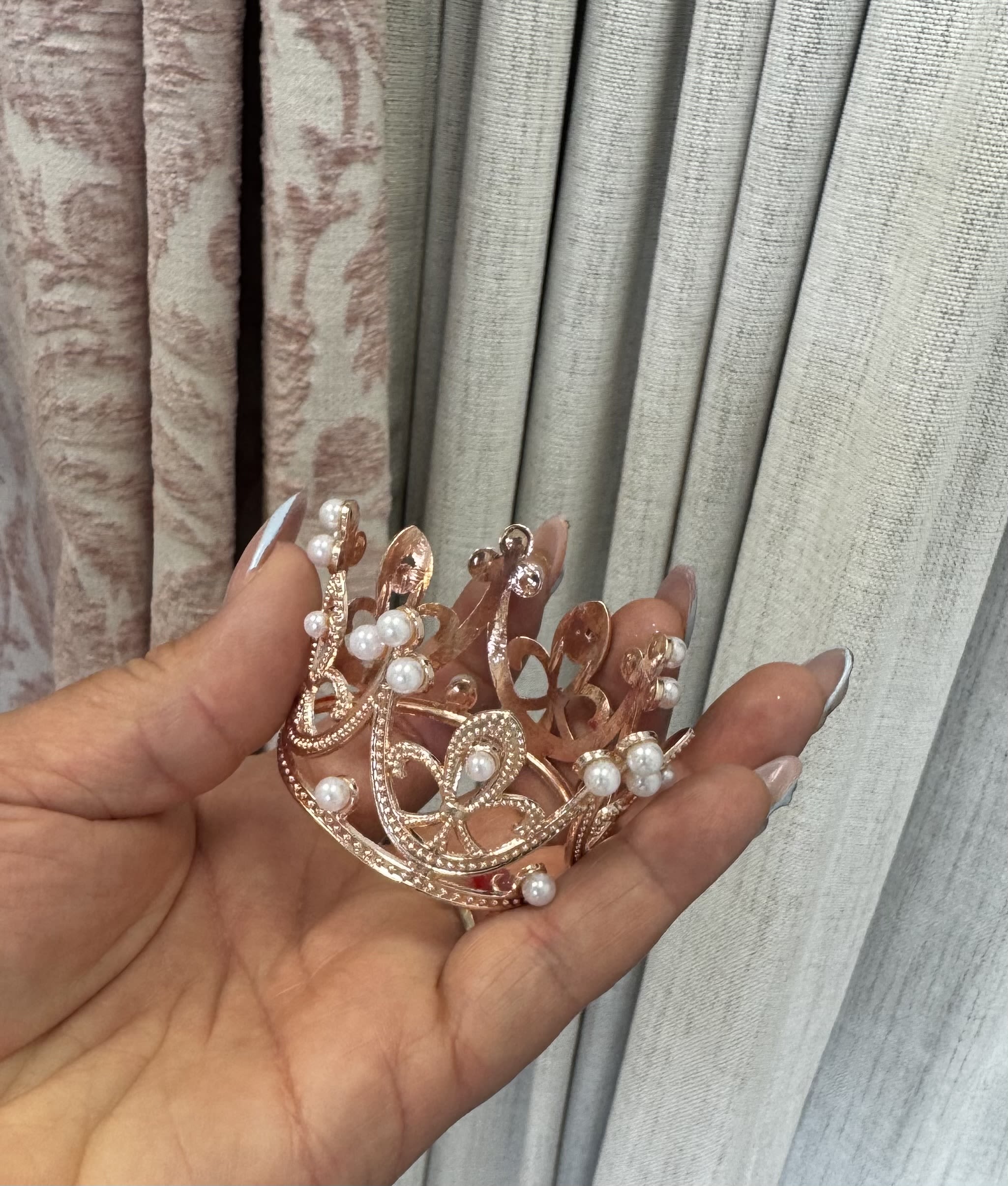 Hand holding a small rose-gold jeweled crown