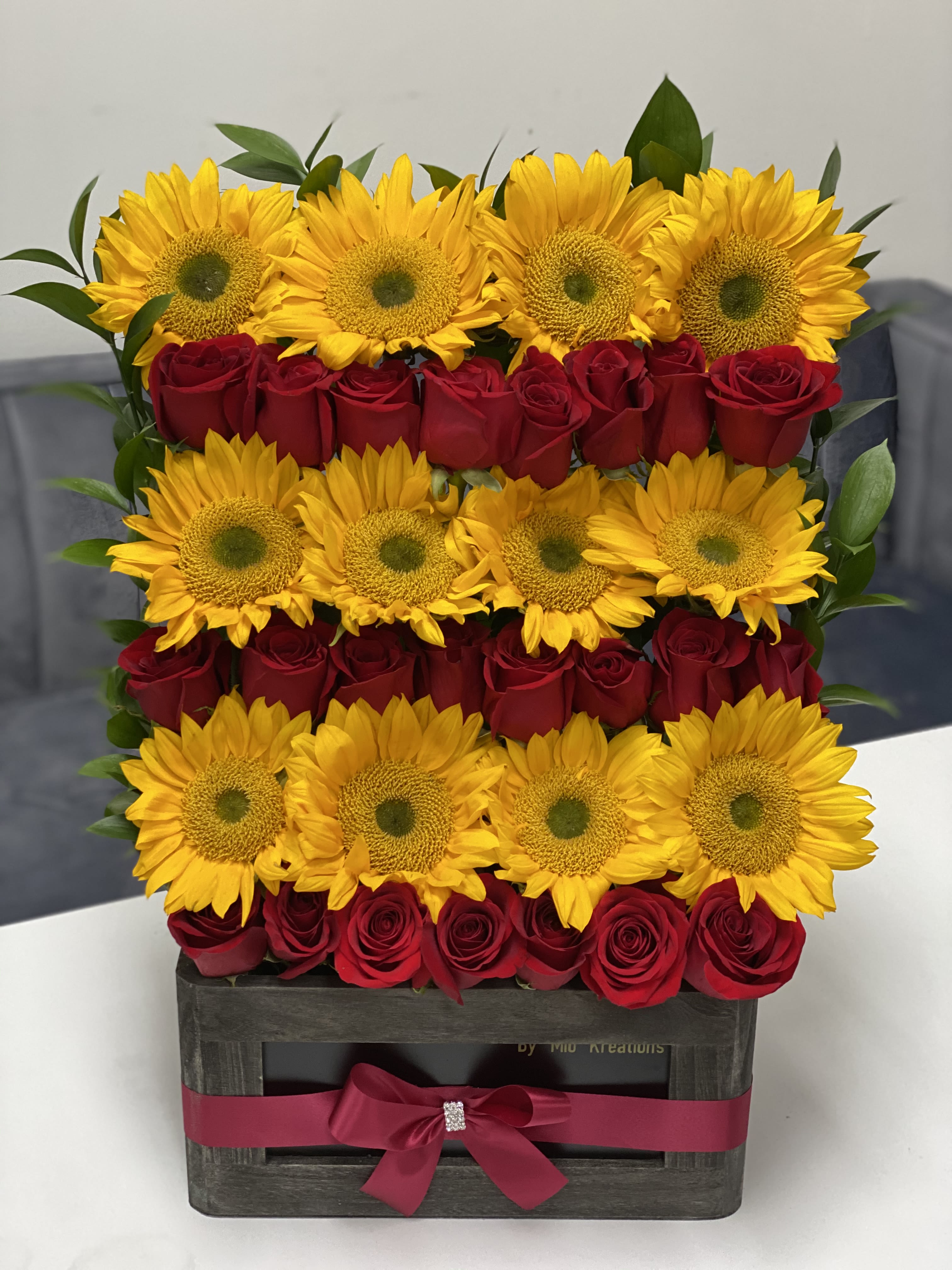 Sunflowers and red roses arranged in a wooden box with a pink ribbon