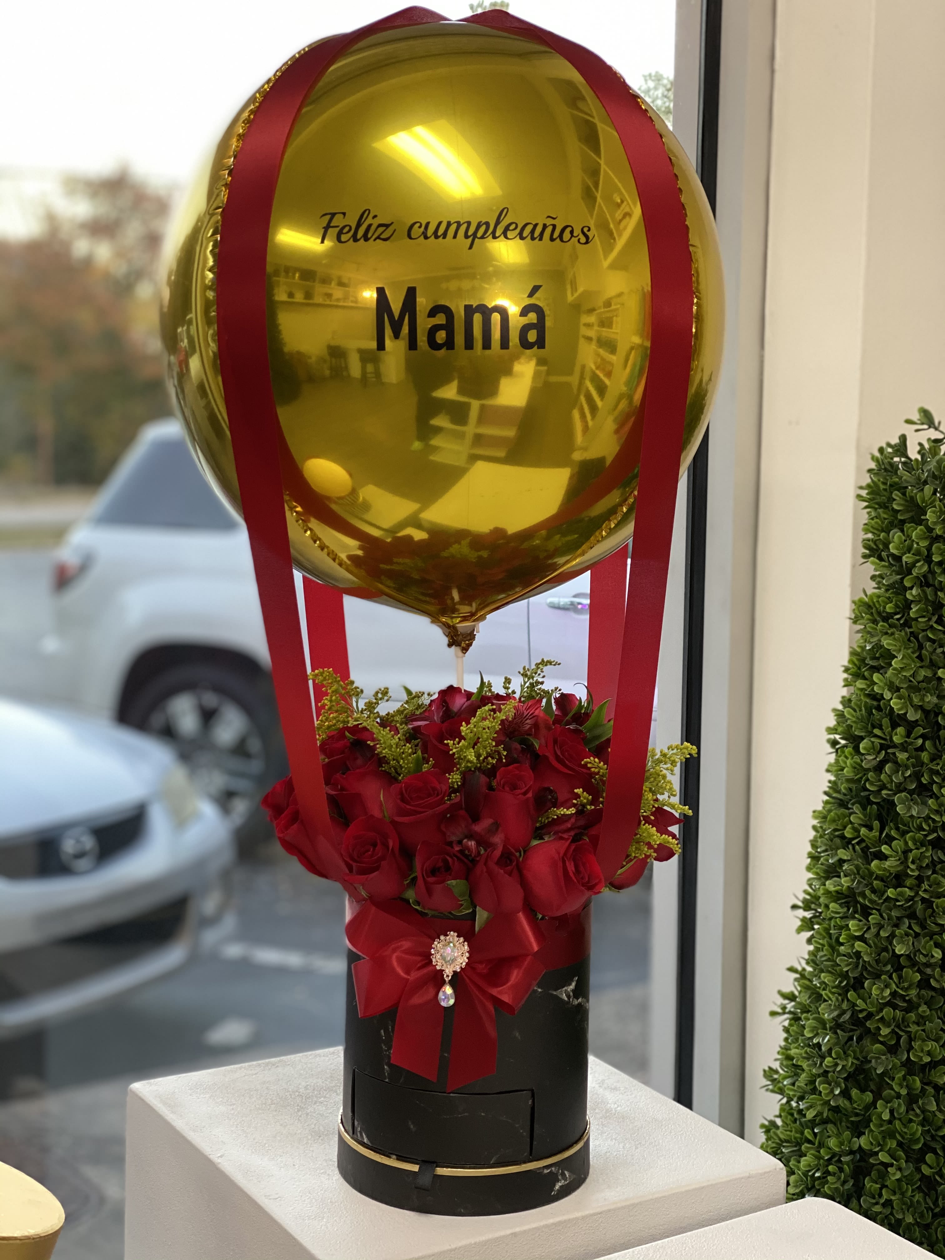 Gold balloon above red roses in a black box with a red bow
