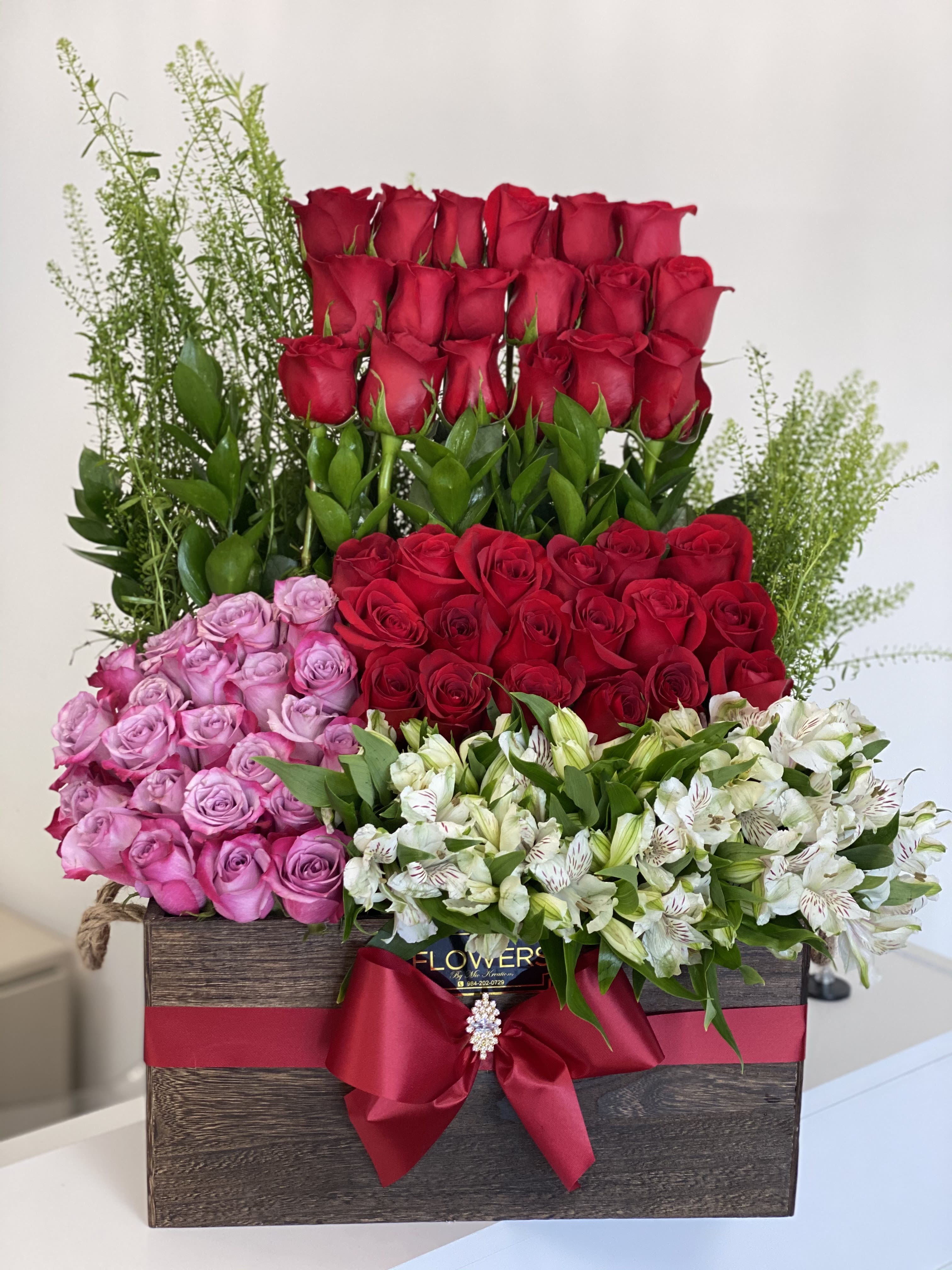 Large box arrangement of red, pink, and white roses with greenery