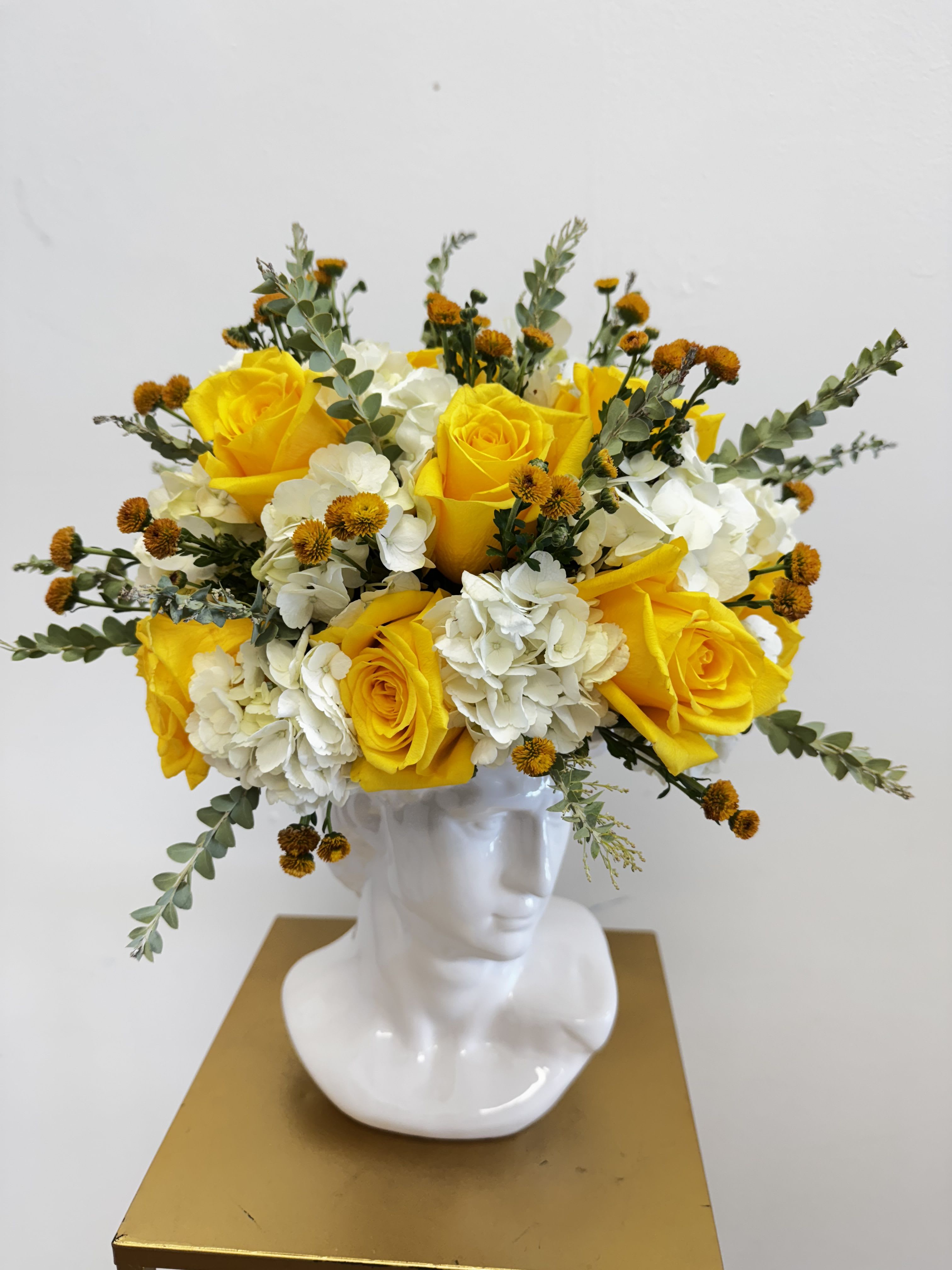 Yellow roses and white hydrangeas arranged in a white bust vase