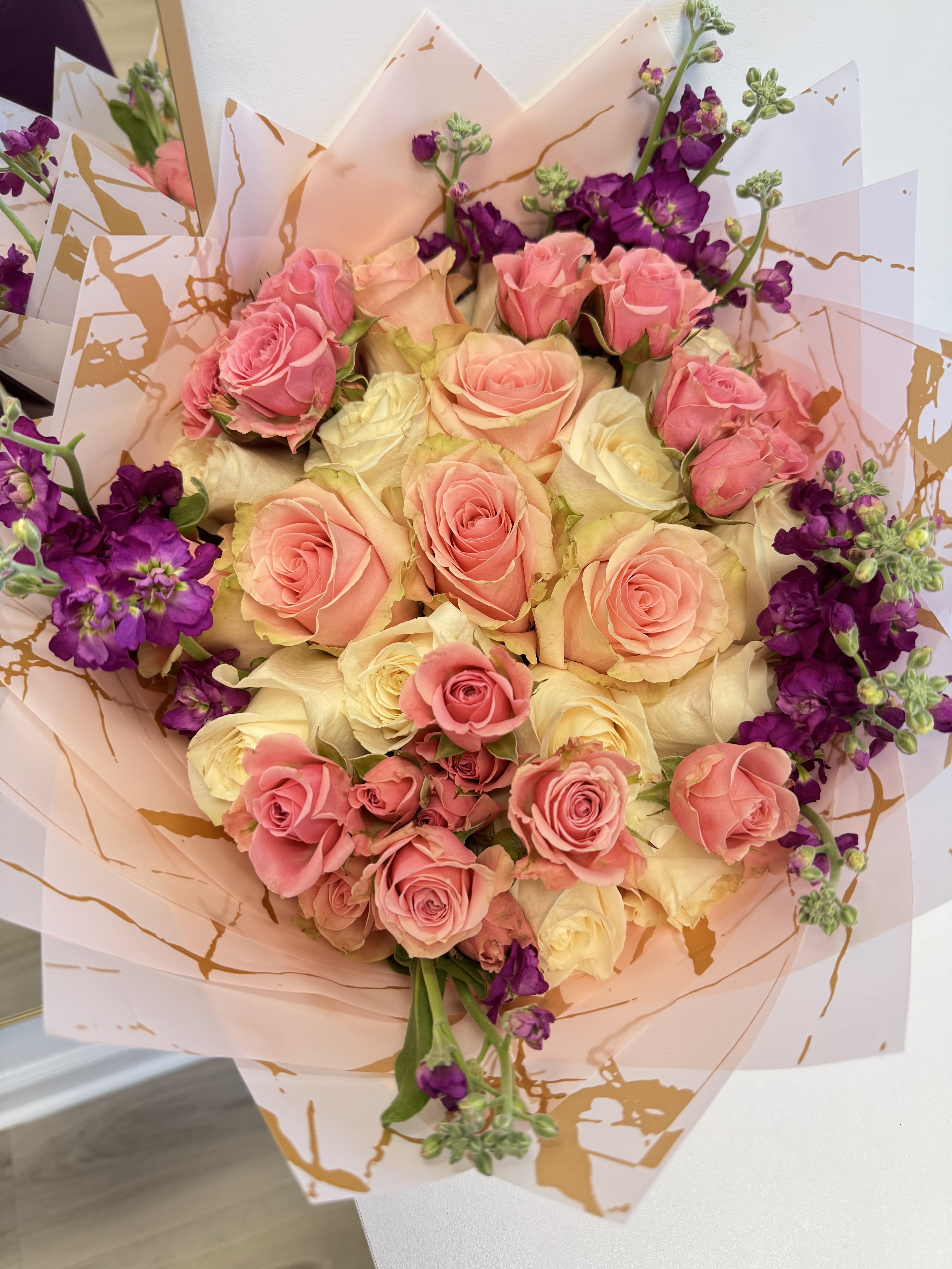 Bouquet of pink and cream roses with purple flowers in decorative wrap