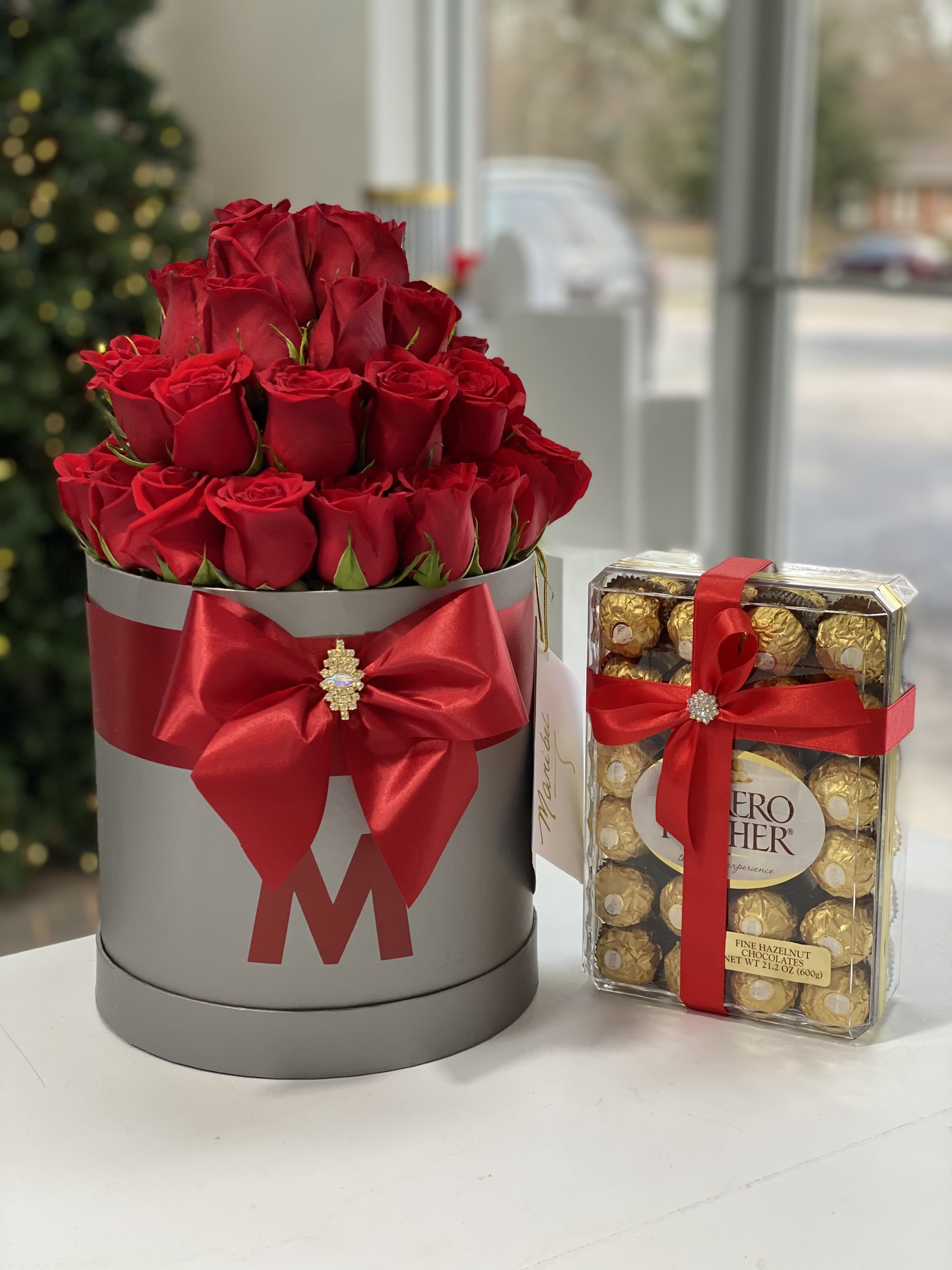 Red roses in a gray hatbox beside a box of chocolates tied with red ribbon