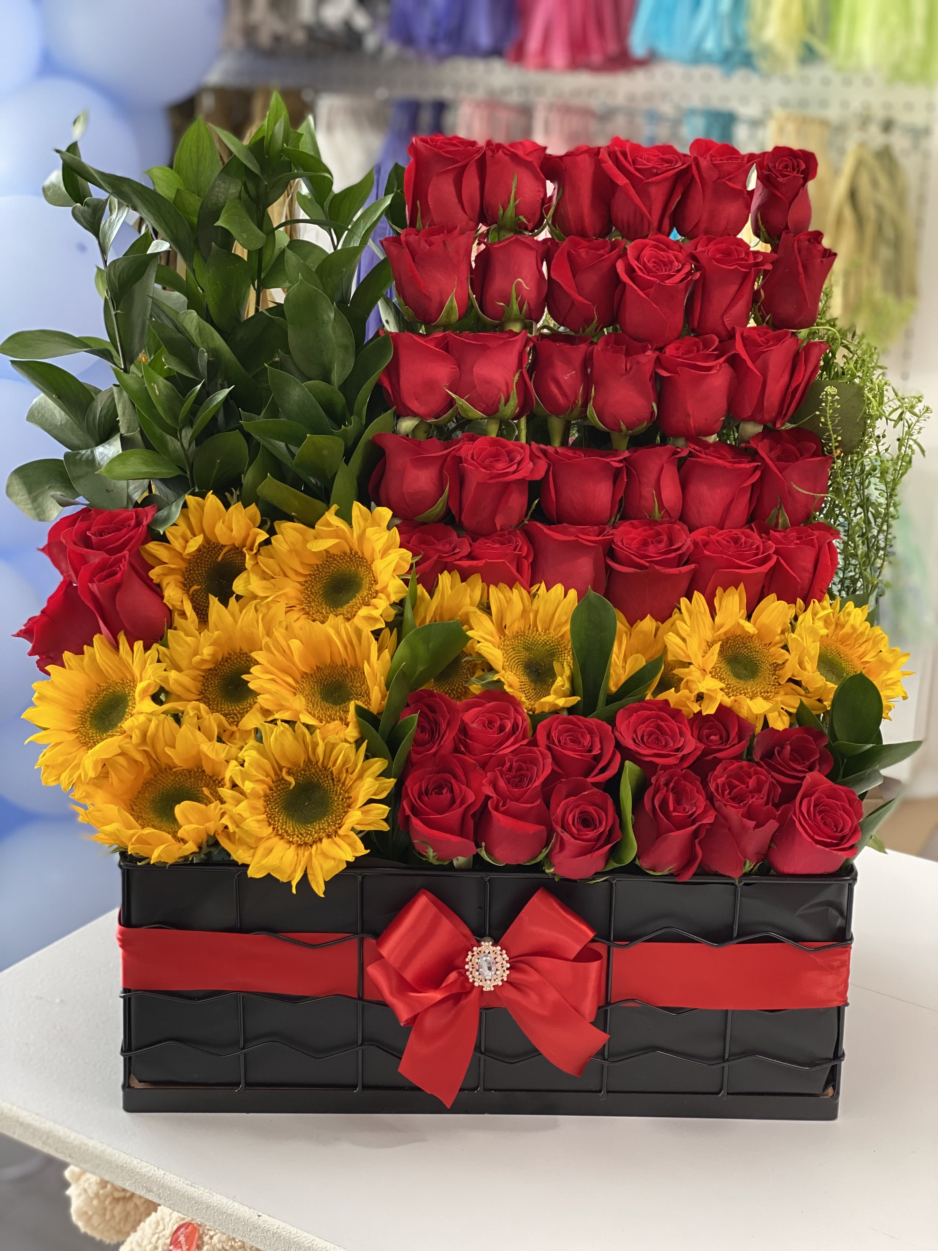 Red roses and yellow sunflowers arranged in a black box with a red ribbon
