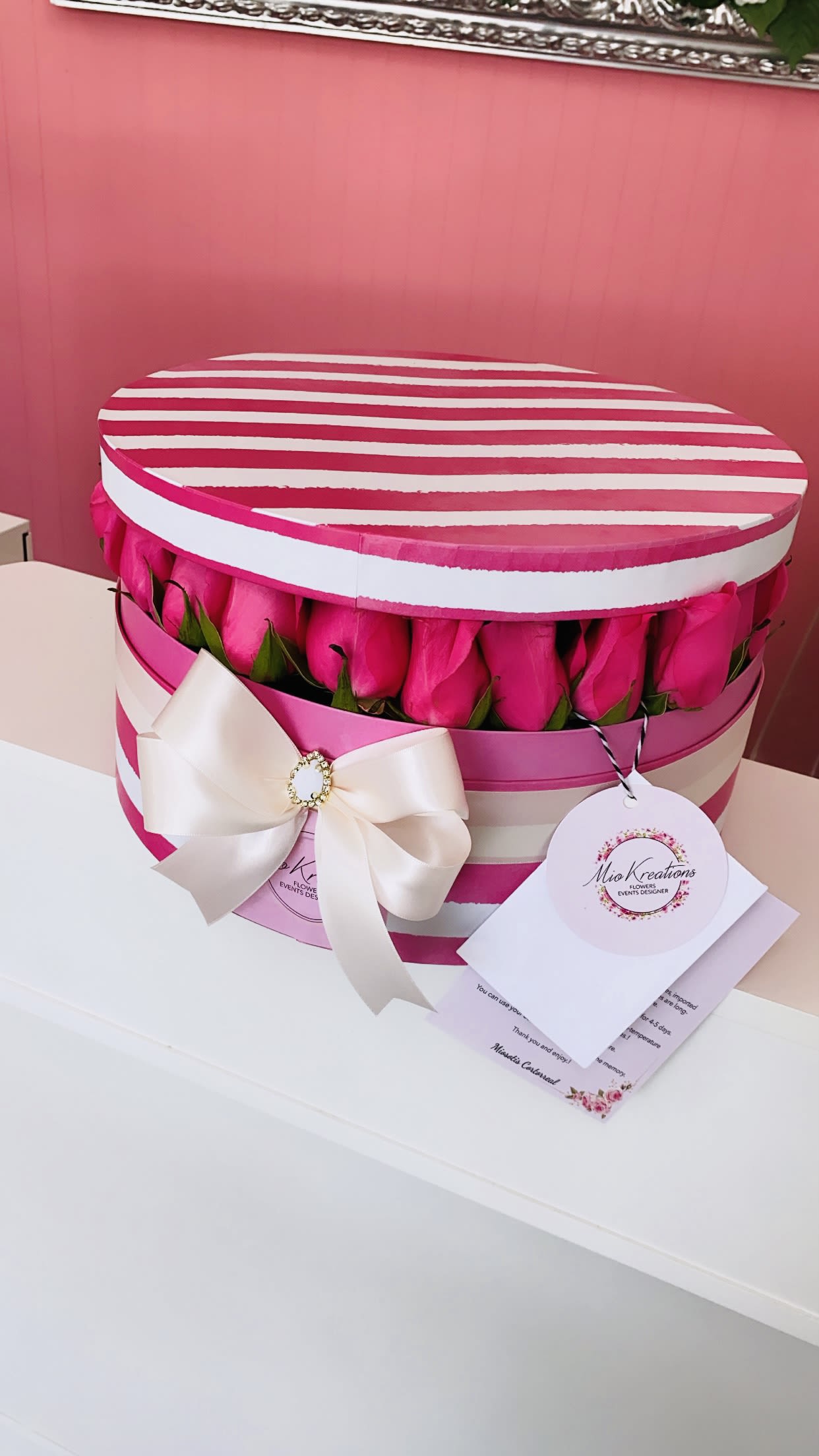 Pink roses arranged in a striped round gift box with a white bow