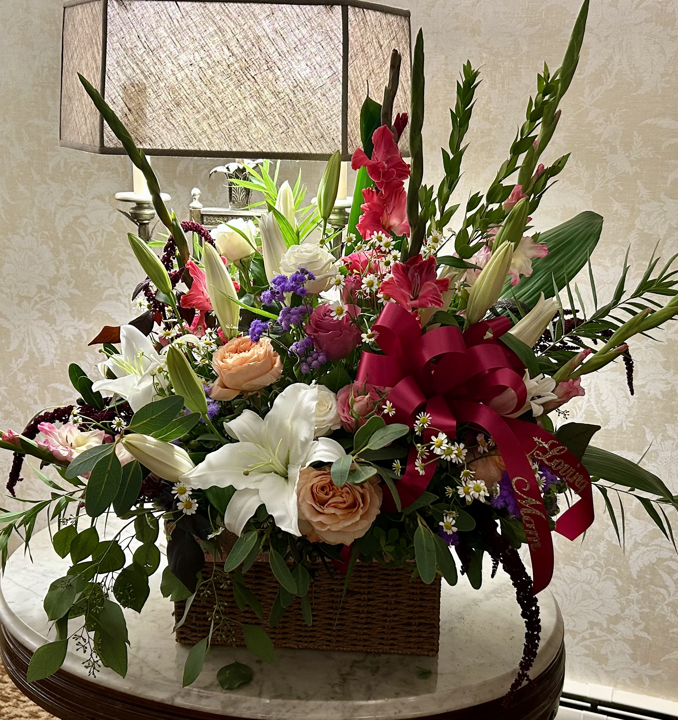 Large mixed flower arrangement in a wicker basket with a red ribbon