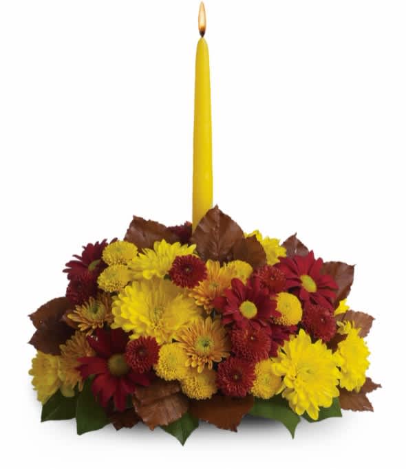 Yellow taper candle in a low arrangement of red and yellow chrysanthemums