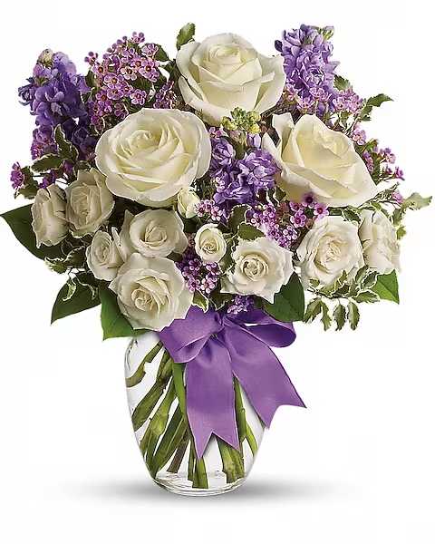 White roses and purple flowers in a glass vase with a purple ribbon