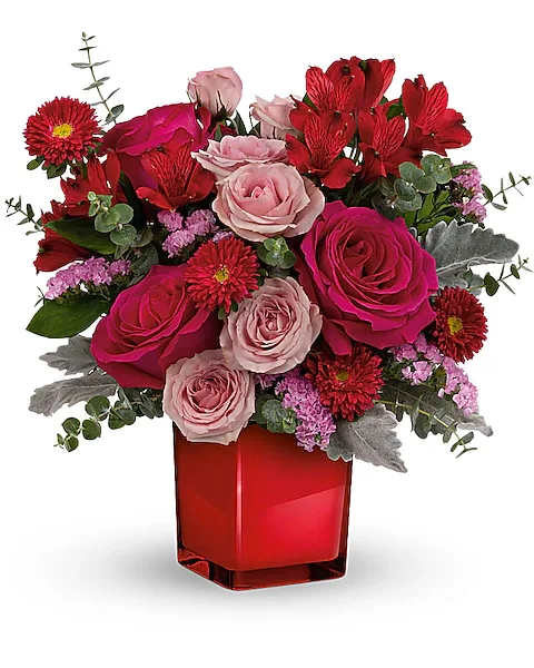 Red and pink mixed flower arrangement in a red glass vase