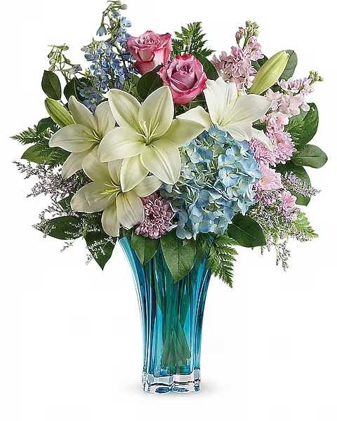 Bouquet of lilies, roses, hydrangeas, and blue flowers in a blue glass vase