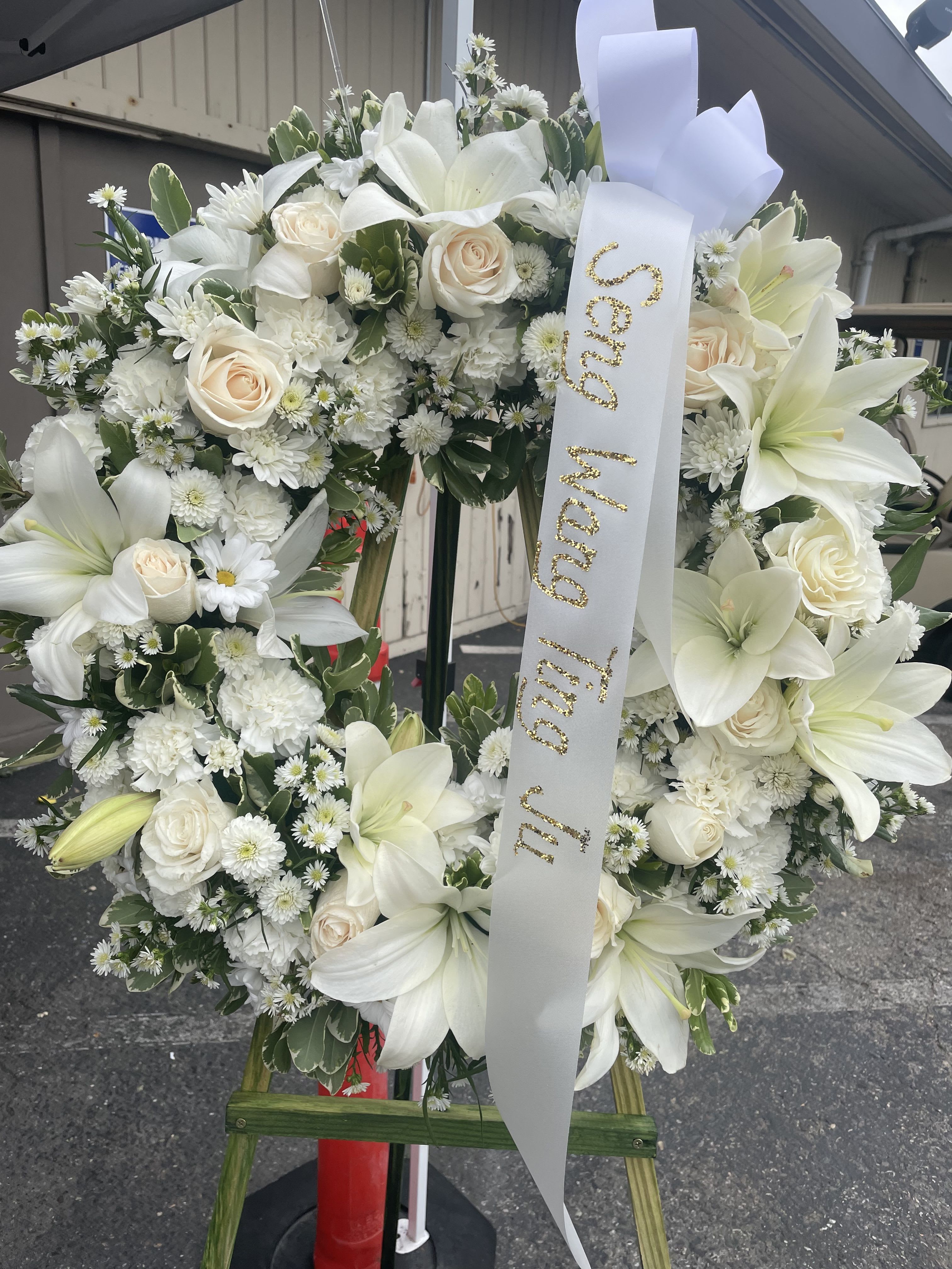 White floral funeral wreath with lilies, roses, and a memorial ribbon