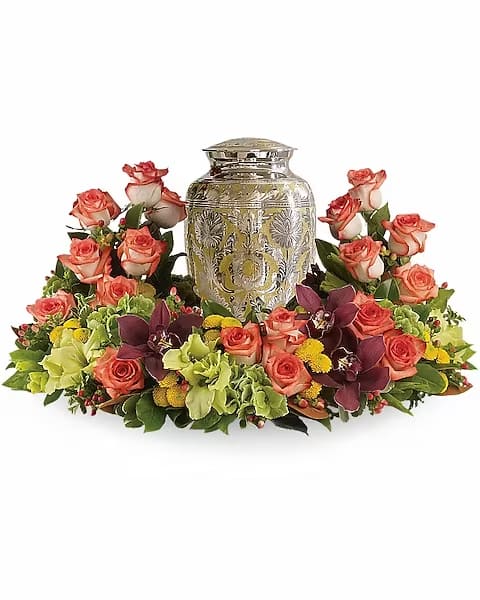 Coral roses and orchids arranged around a decorative urn