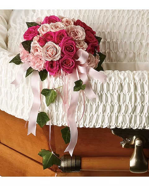 Pink and blush rose bouquet with ribbon drape on a white casket