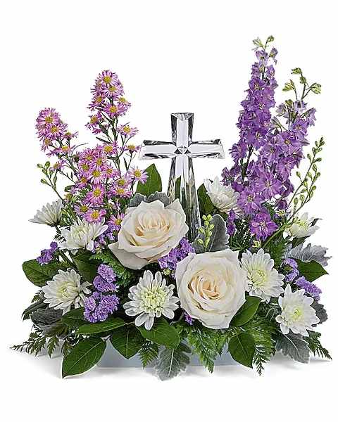 White roses and purple flowers arranged around a silver cross.