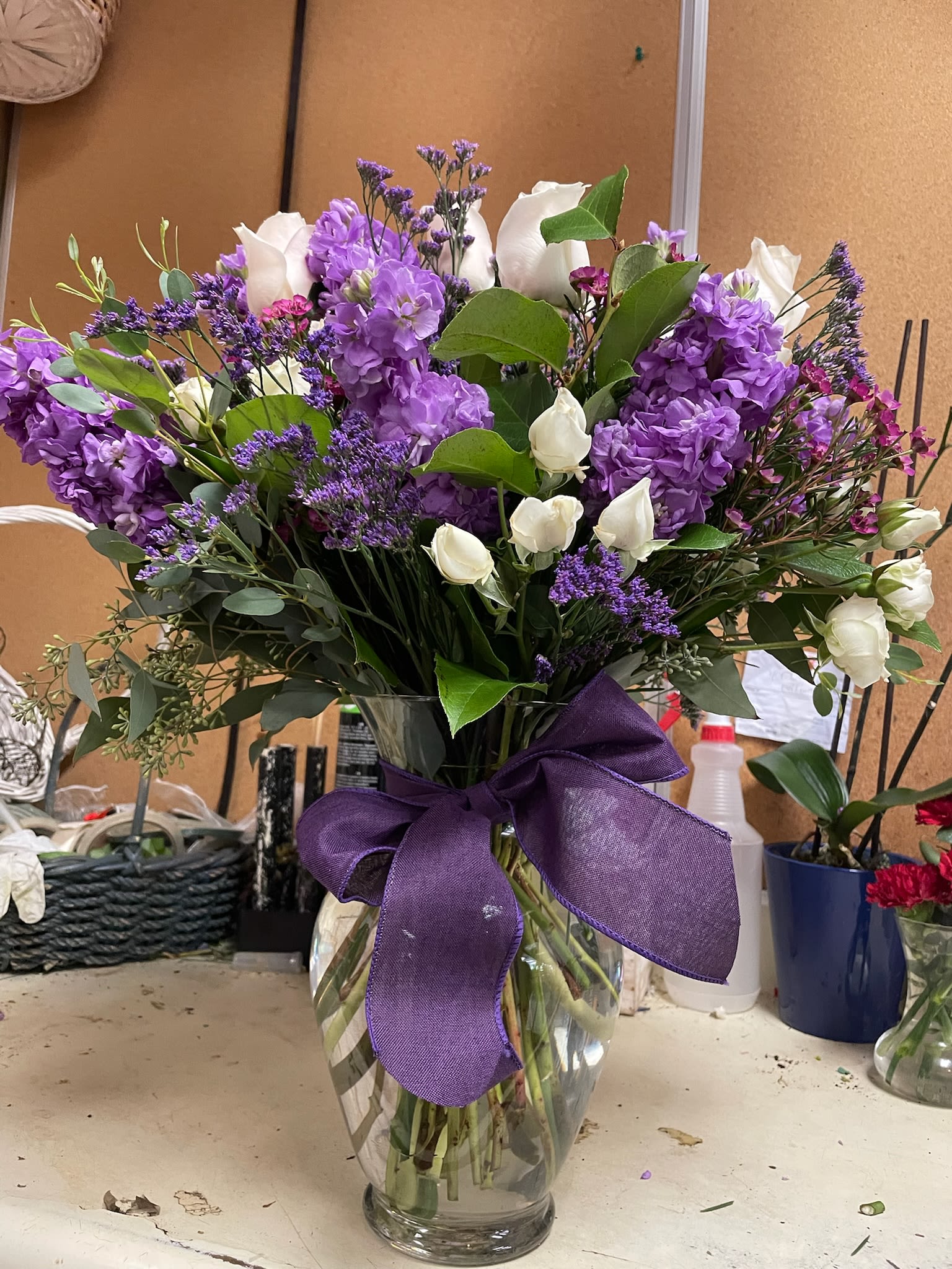 Purple and white flower bouquet in a clear glass vase with a purple ribbon
