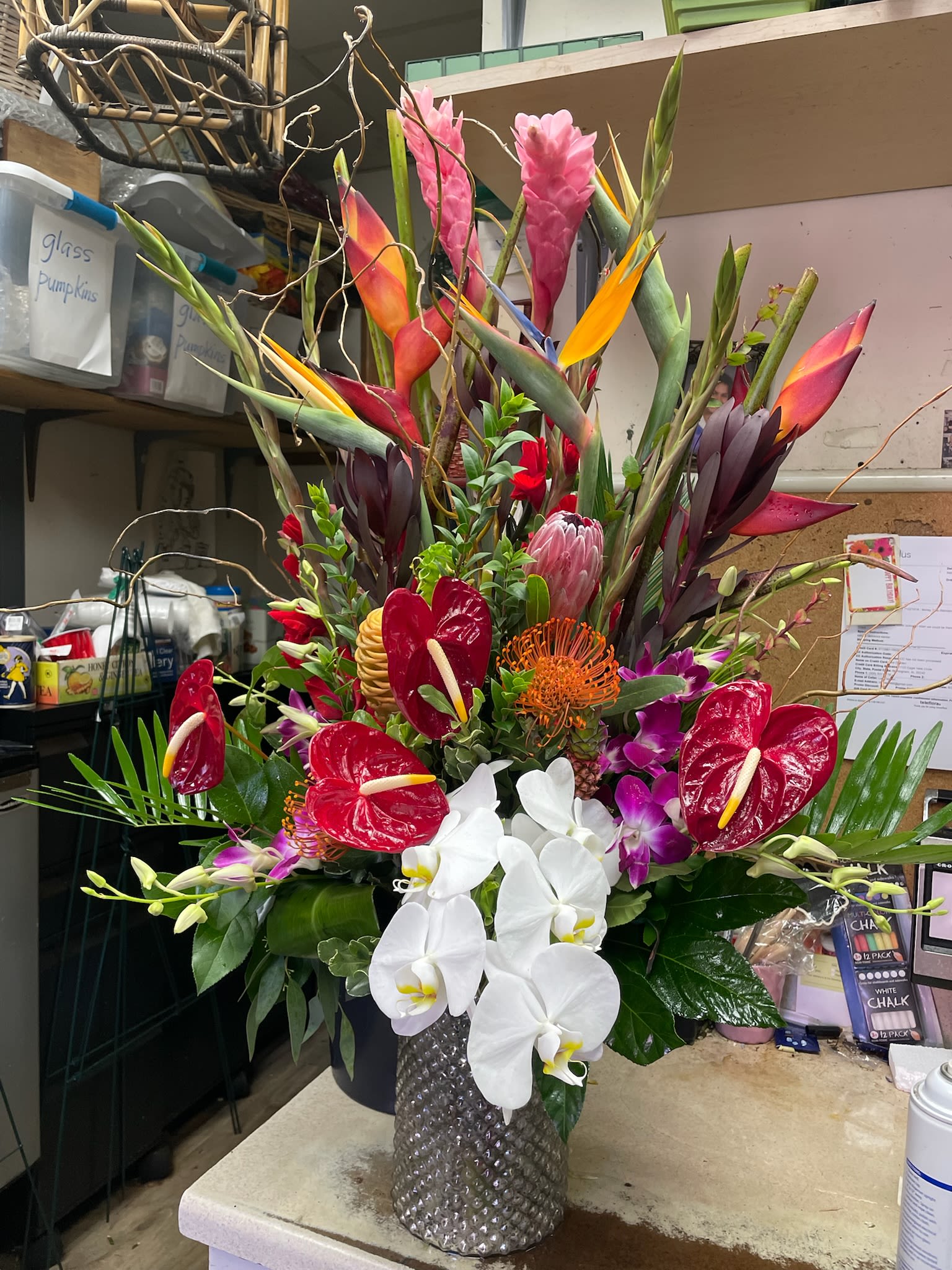 Tall tropical arrangement with orchids, anthuriums, and bird-of-paradise in a textured vase
