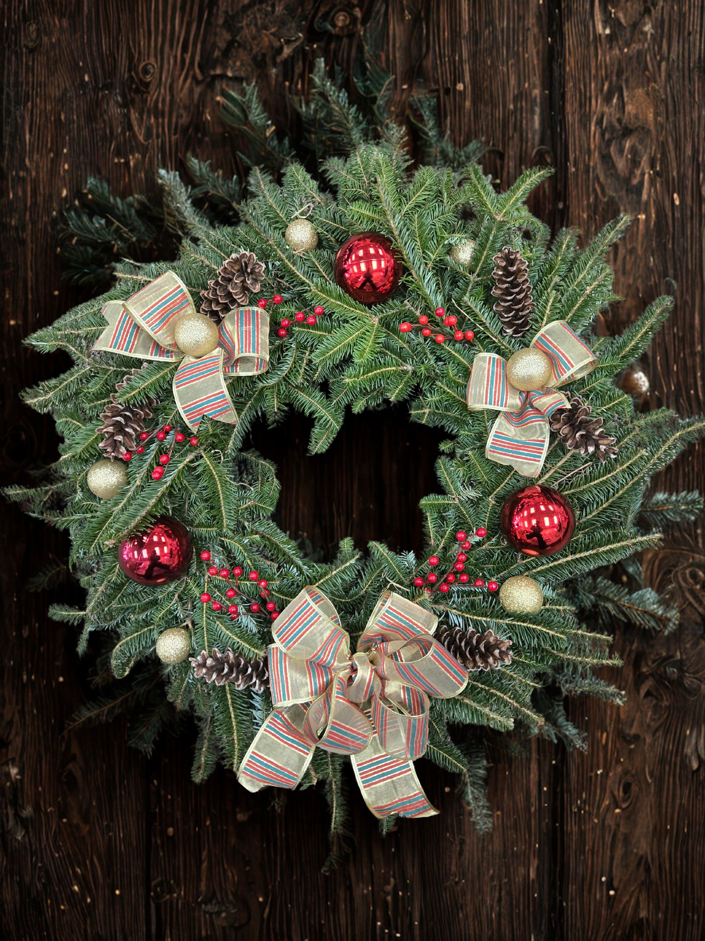 Christmas wreath with pine branches, red ornaments, pinecones, and striped bows