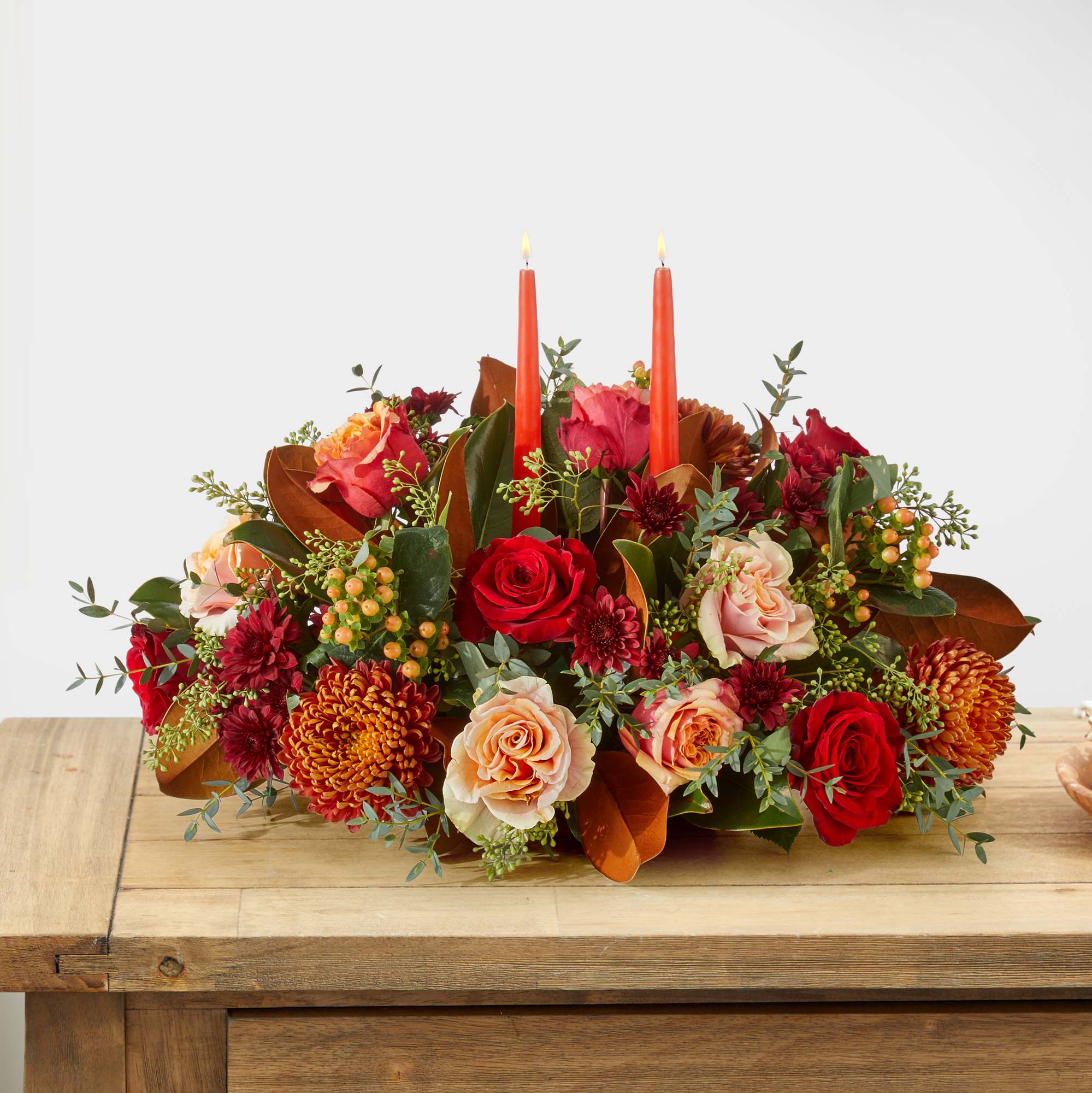 Low floral centerpiece with red and peach roses and two orange taper candles