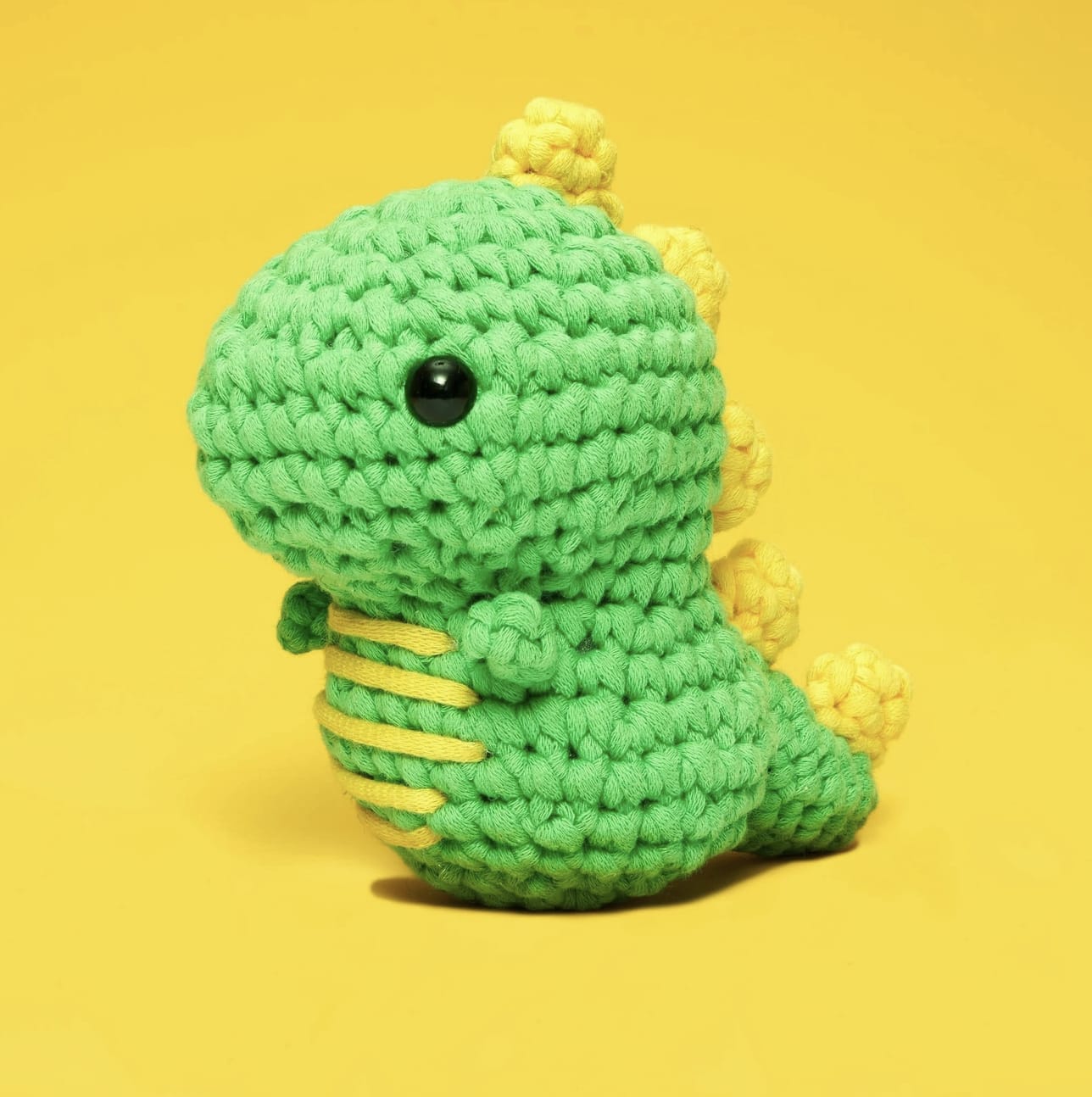 Crocheted green dinosaur plush with yellow accents on a yellow background