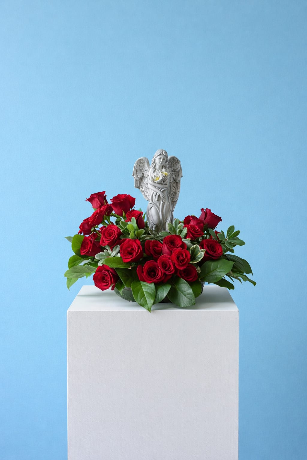 Red roses arranged around a small angel figurine on a white pedestal