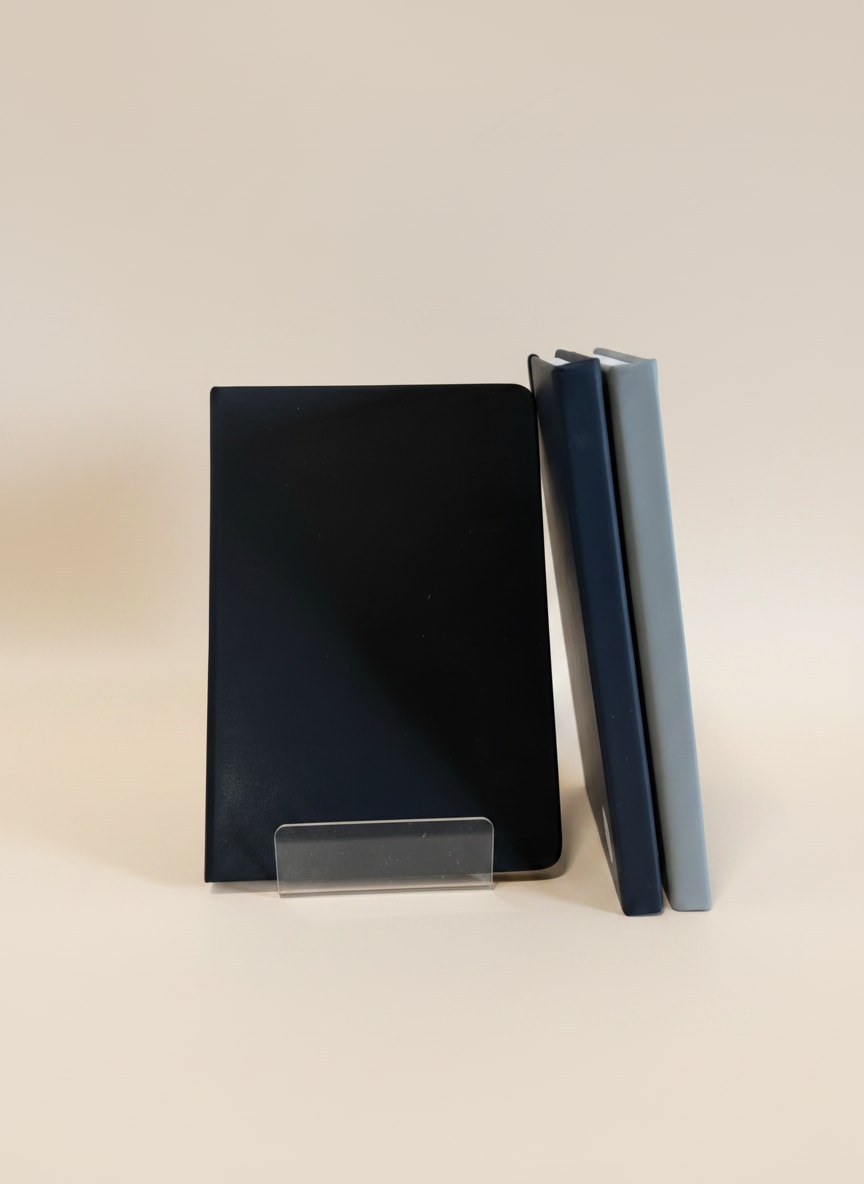 Three plain rectangular notebooks or journals in dark blue, black, and light gray