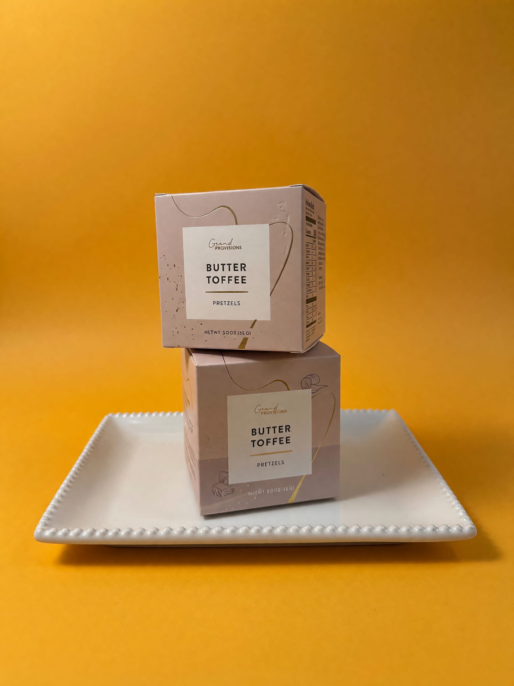 Two butter toffee pretzel boxes stacked on a white tray.