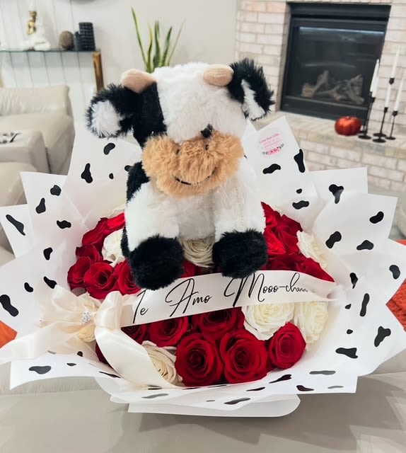 Round bouquet of red and white roses wrapped in cow-print paper with a plush cow toy on top.