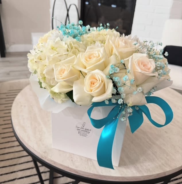 Cream roses and white flowers in a white gift box with a blue ribbon