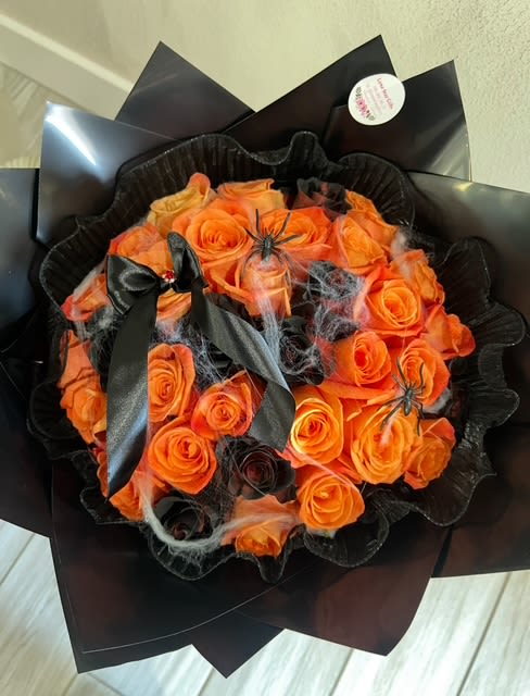 Orange rose bouquet wrapped in black paper with ribbon and spider decorations