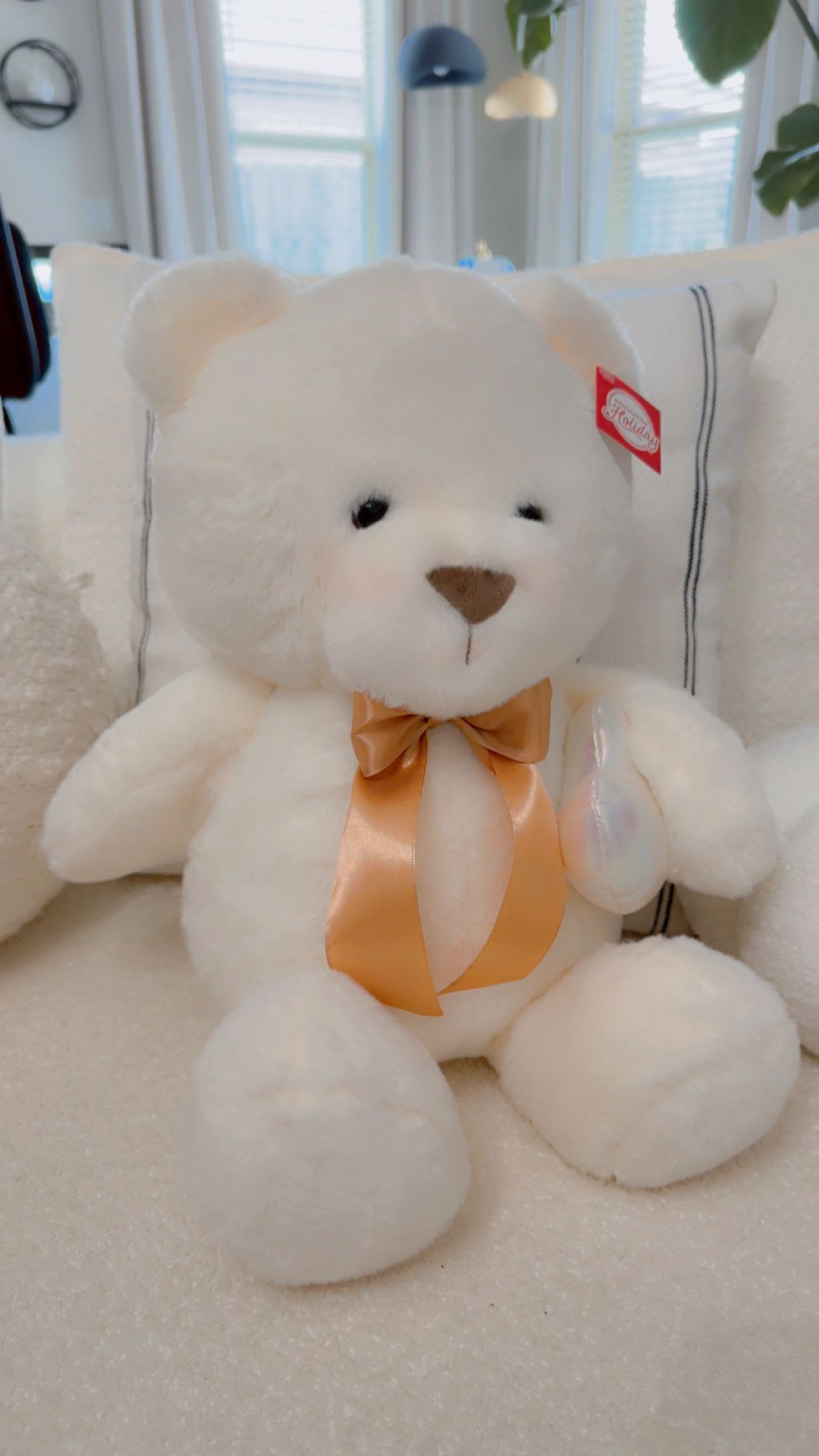 White teddy bear with an orange ribbon sitting on a couch