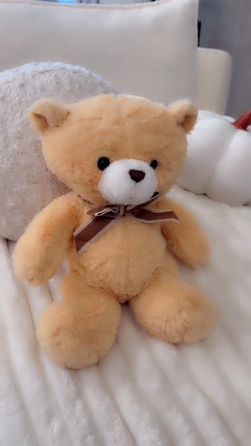 Plush teddy bear with a ribbon bow sitting on a bed
