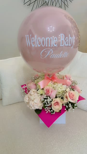 Pink balloon above a pastel flower arrangement with a baby name message