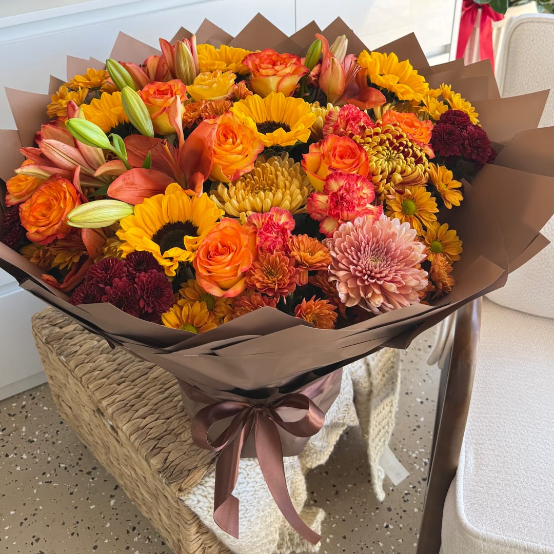 Bouquet of orange and yellow flowers wrapped in brown paper with a ribbon