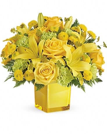 Yellow roses and lilies arranged in a square glass vase
