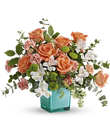 Peach roses and white flowers in a turquoise glass vase