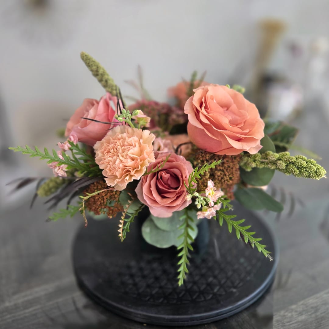 Peach and pink rose arrangement in a black vase with greenery