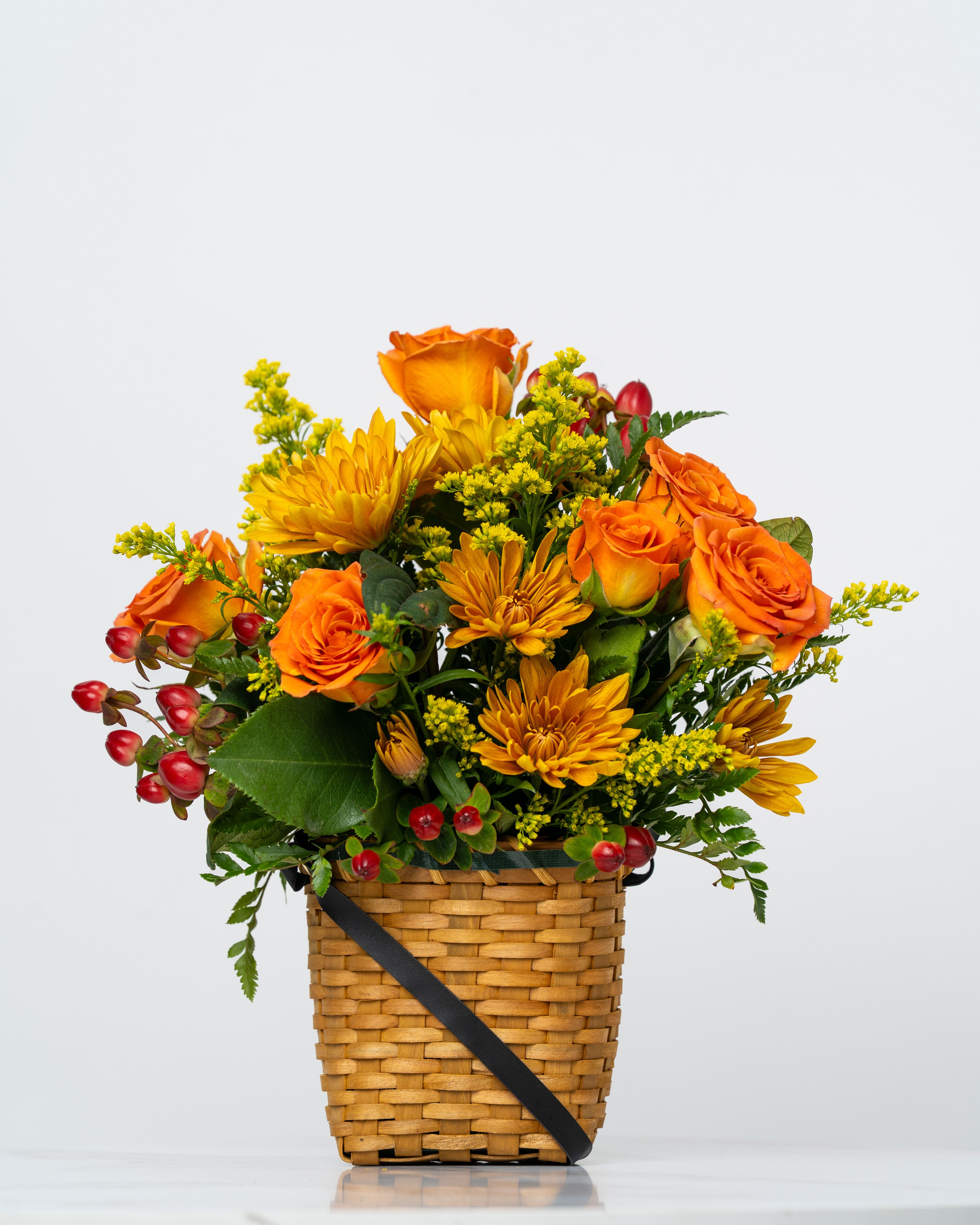 Orange roses and yellow mums in a woven basket with red berries