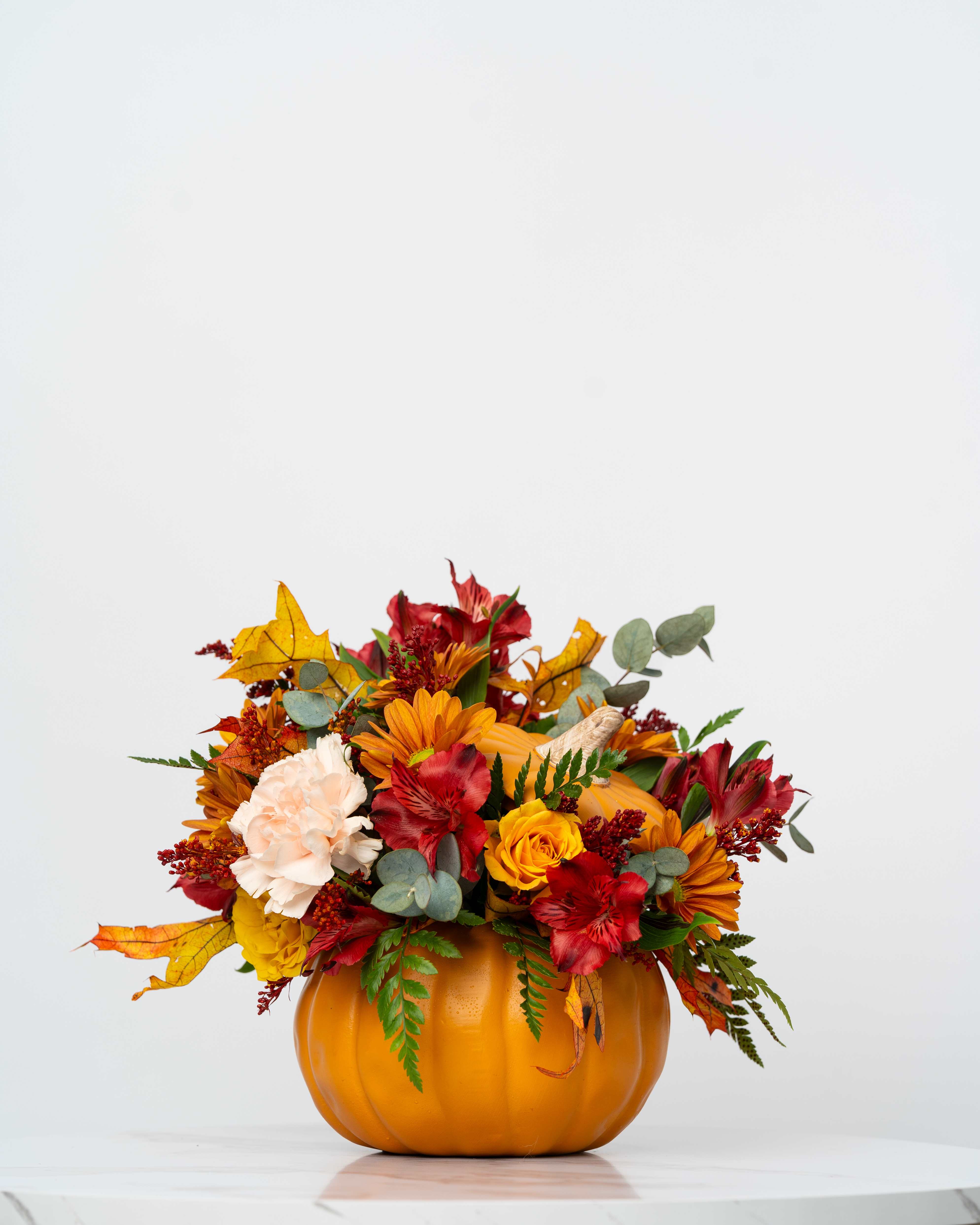 Autumn flower arrangement in a pumpkin-shaped container with red, orange, and cream blooms