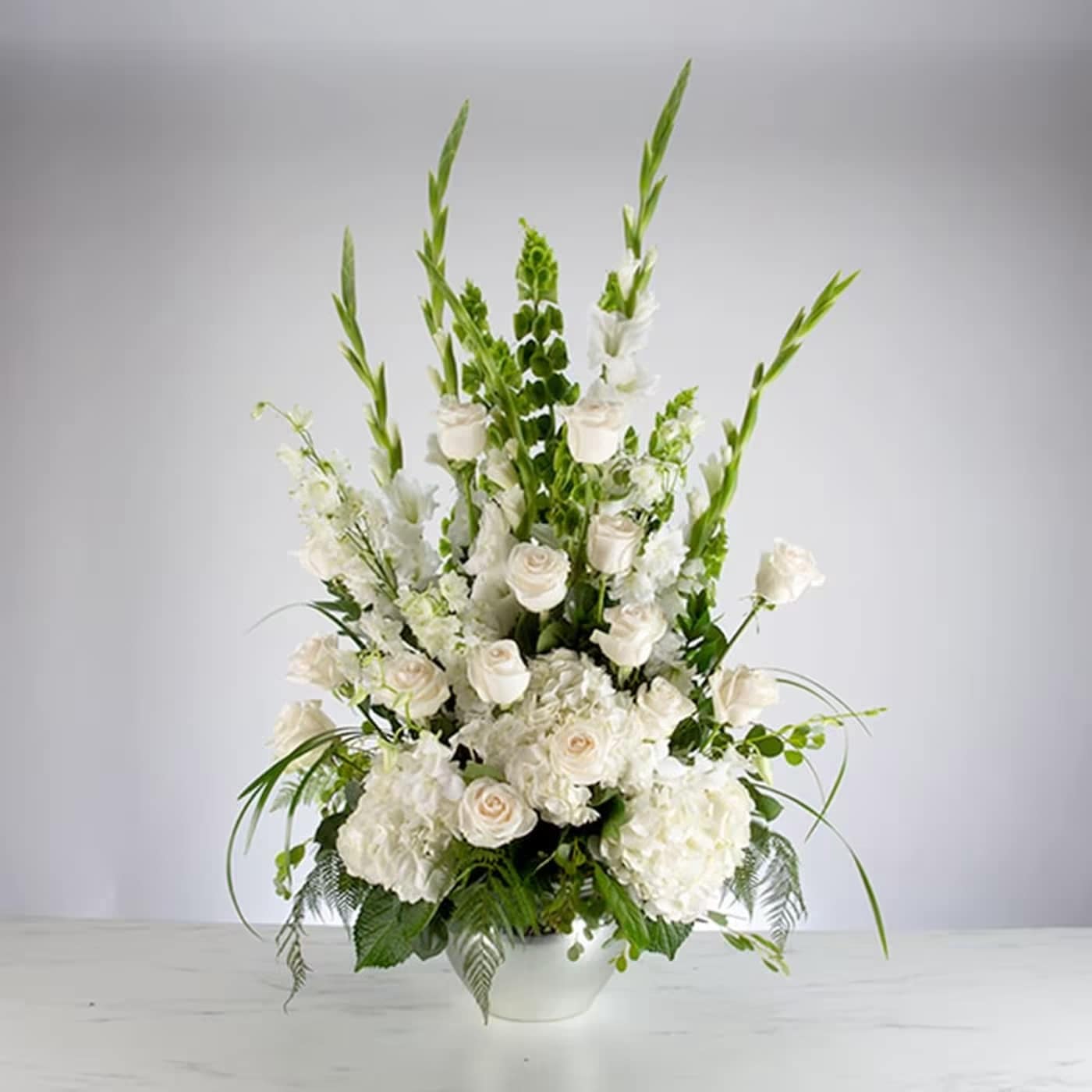 White floral arrangement in a white vase with tall green accents