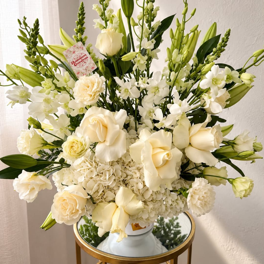 Cream and white floral arrangement in a white vase with tall green buds