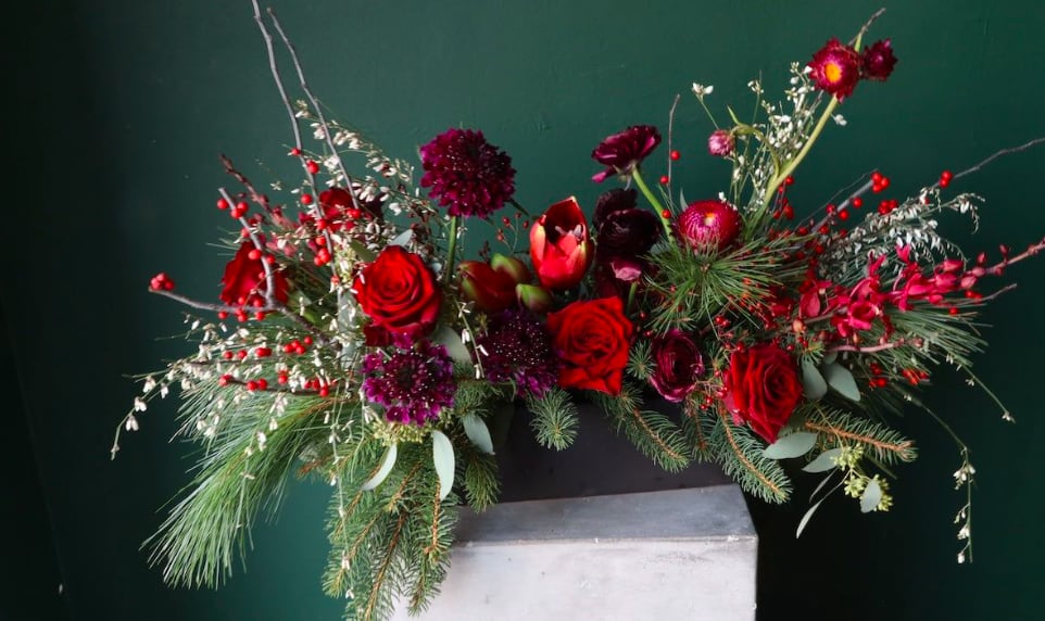 Red roses and burgundy flowers in a low arrangement with pine branches